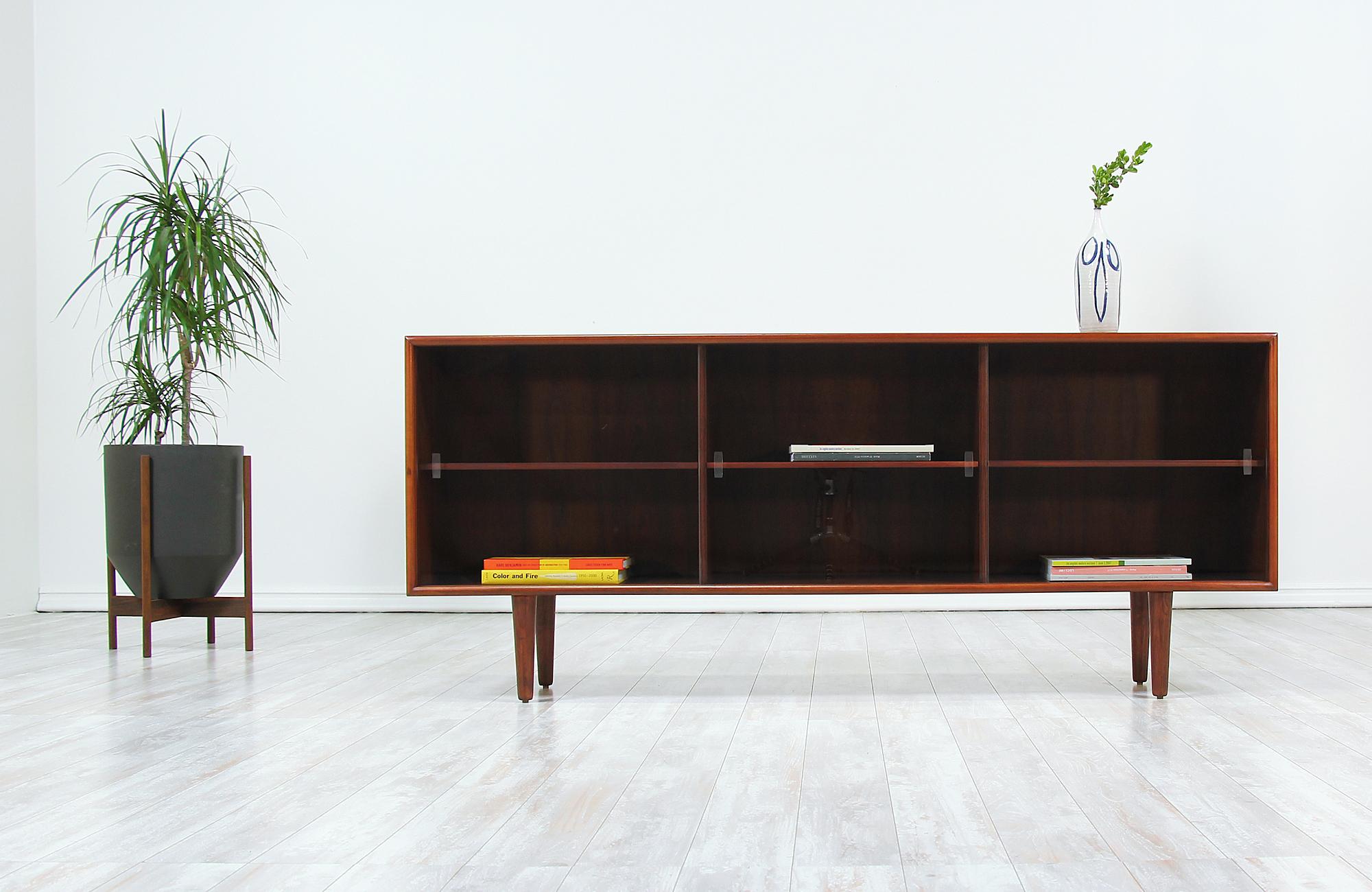 Stylish Danish credenza designed and manufactured by H.P. Hansen Møbelindustri in Denmark, circa 1960s. This sleek design features a rosewood case sitting on four tapered legs with its original sliding glass doors. The interior is comprised of three