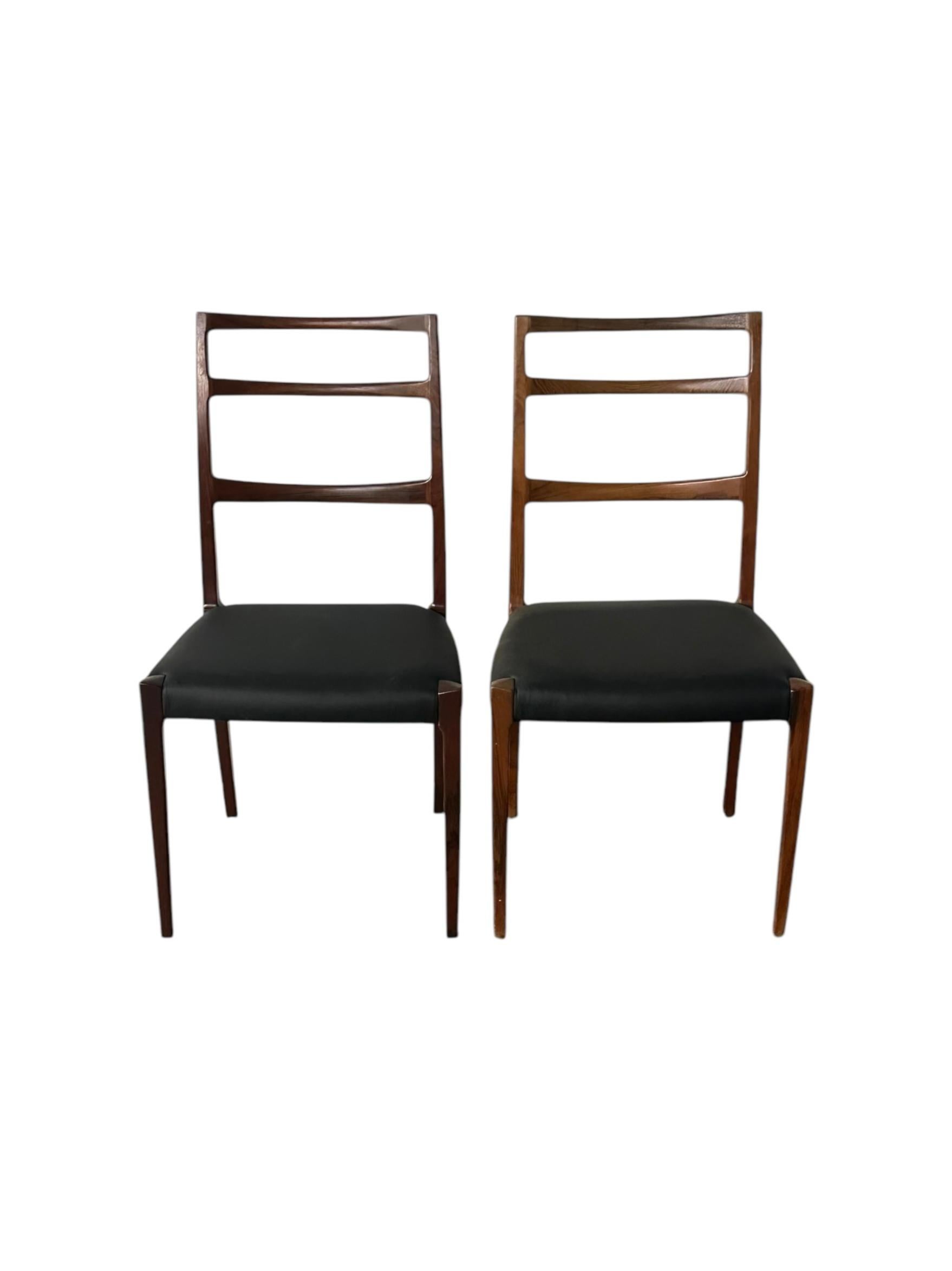 Pair of elegant ladder back dining chairs. Imported from Denmark and exhibiting classic Danish modern refinement in silhouette and form. Constructed of solid rosewood and outfitted with new leather seats. Beautiful nuance in color and grain patterns.