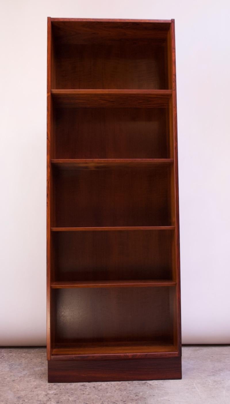 Danish plinth-base bookcase in rosewood by Carlo Jensen for Poul Hundevad (1960s, Denmark). Tall, but narrow footprint whose minimal design is nicely contrasted by vivid rosewood grain and nicely finished chamfered edge shelves.
Conservatively