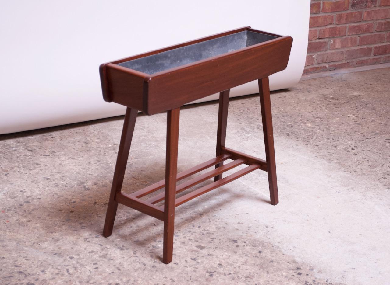 Indoor Danish planter in solid rosewood with the original insert present. The bottom slatted rack provides additional storage for accessories.
Rosewood has been newly refinished; the insert shows water rings / general wear from use.
Measures: H