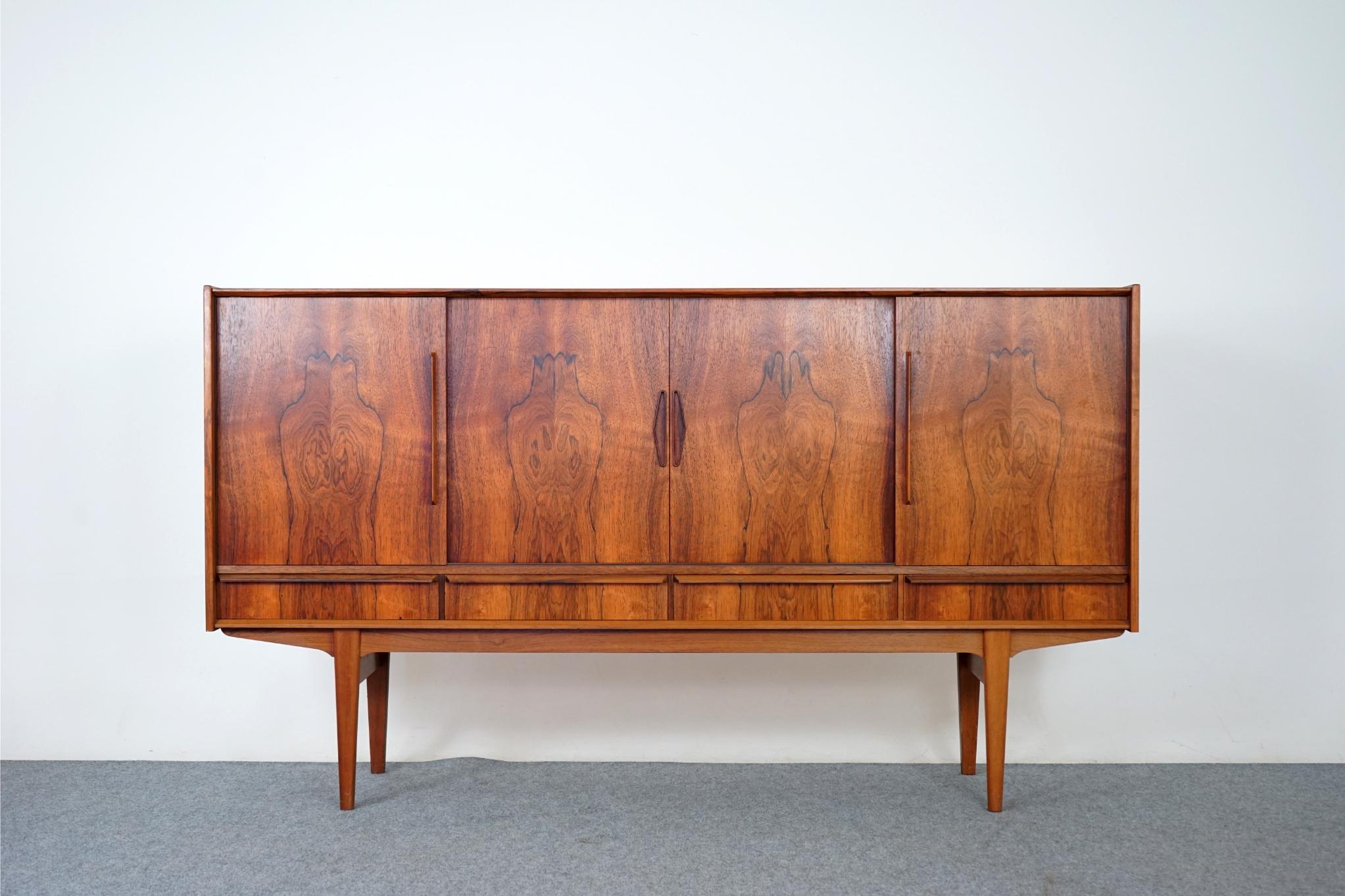 Rosewood sideboard, circa 1960's. Clean, simple lined design highlights the exceptional book-matched veneer throughout. Sliding doors and exterior drawers offers ample storage to hide away clutter, show off your favourite things. Interior bays are
