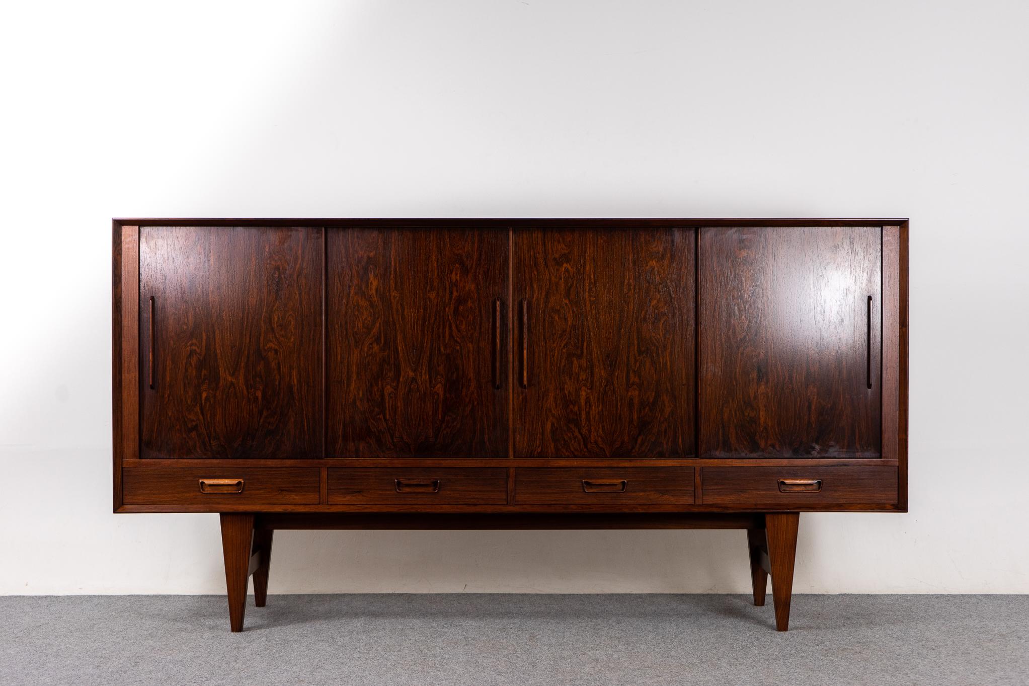 Rosewood Danish modern sideboard with integrated bar, circa 1960's. Clean lined design with exceptional book-matched veneer! Sliding doors and drawers offers ample storage for all your needs. 3 interior bays are outfitted with 6 adjustable shelves.