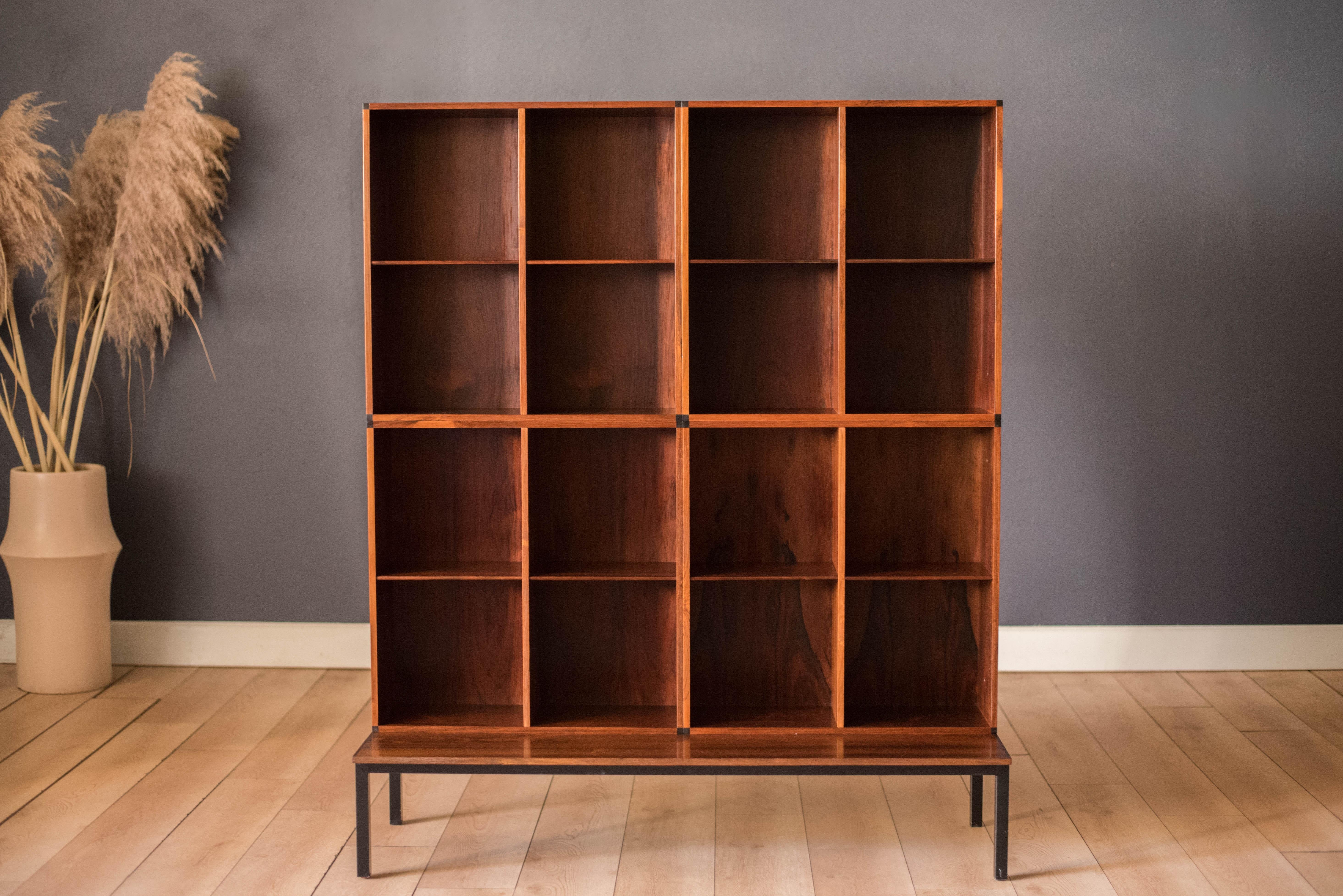 Mid century modern three piece bookcase set circa 1970's, Denmark. Features stunning rosewood grains throughout and an open storage display with adjustable shelving. Includes two stacking bookcases and one table supported by a sturdy black metal
