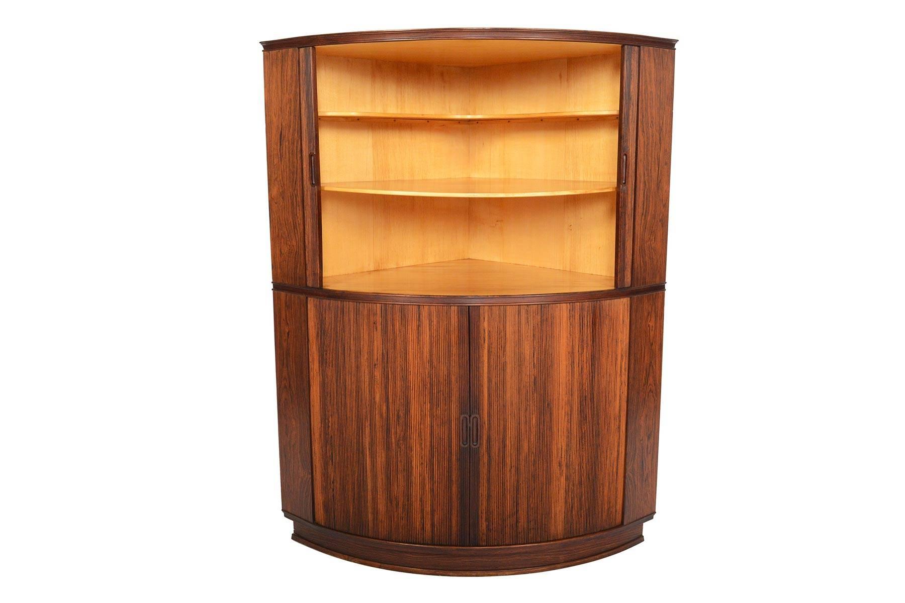 This Danish modern corner cabinet is crafted in Brazilian rosewood and features two tiers of tambour perfection! A wonderful storage piece, doors smoothly open to reveal birch lined interiors and fixed shelves. In excellent original condition with