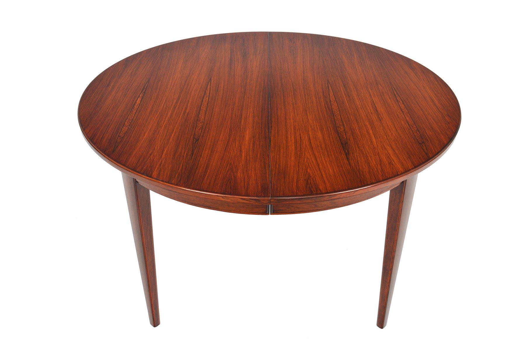 This beautifully simple round dining table was manufactured in Denmark in the 1960s. Book- matched Brazilian rosewood wood grain is banded with a clean and simple line. Table extends to hold an additional leaf and can comfortably seat four to six