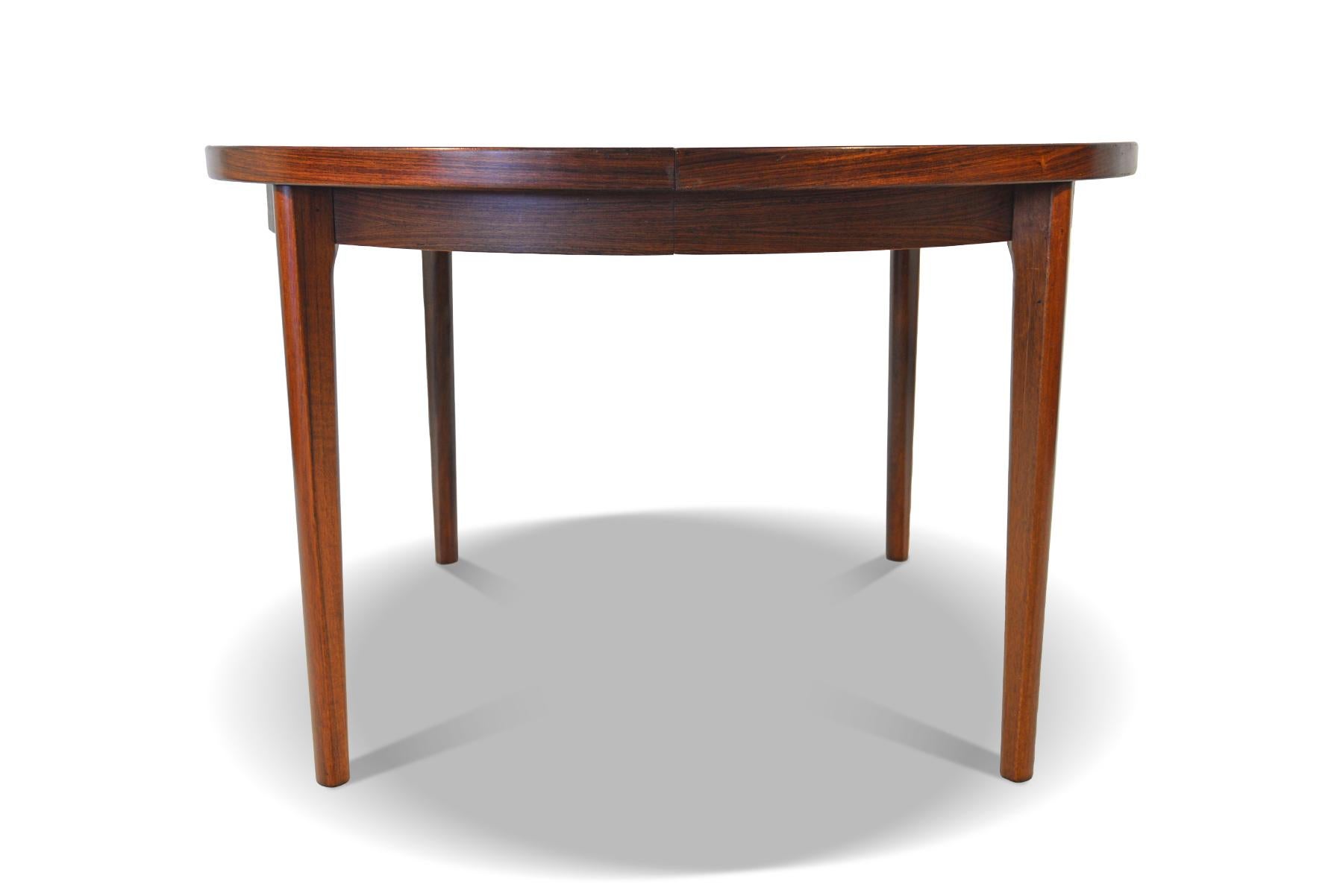 This beautifully simple round dining table was manufactured in Denmark in the 1960s. Book- matched Brazilian rosewood wood grain is banded with a clean and simple line. Table extends to hold two additional leaves and can comfortably seat four to