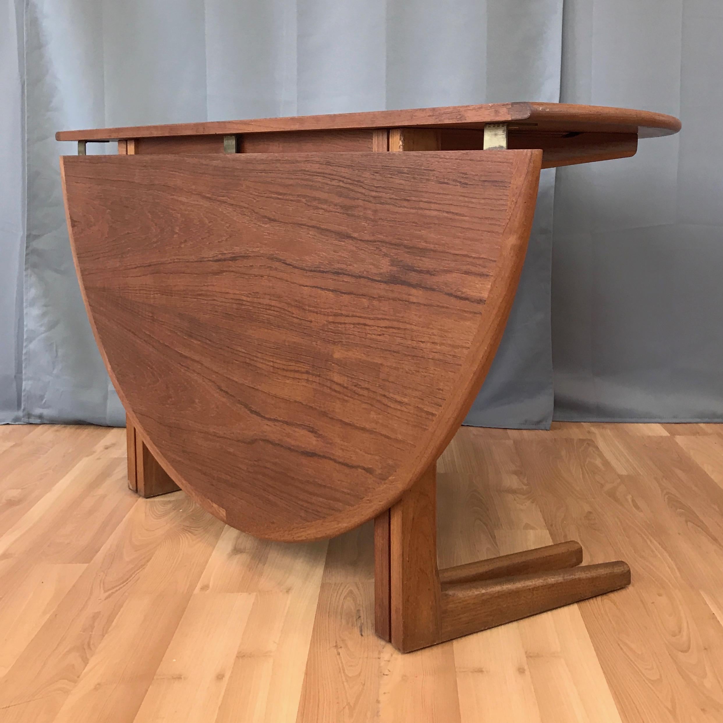 A very handsome and clean 1970s Danish round drop-leaf teak dining table.

Appealingly idiosyncratic design features a top comprised of two slightly unequally sized leaves with bookmatched veneer and a solid bullnose edge. On a broadly supported