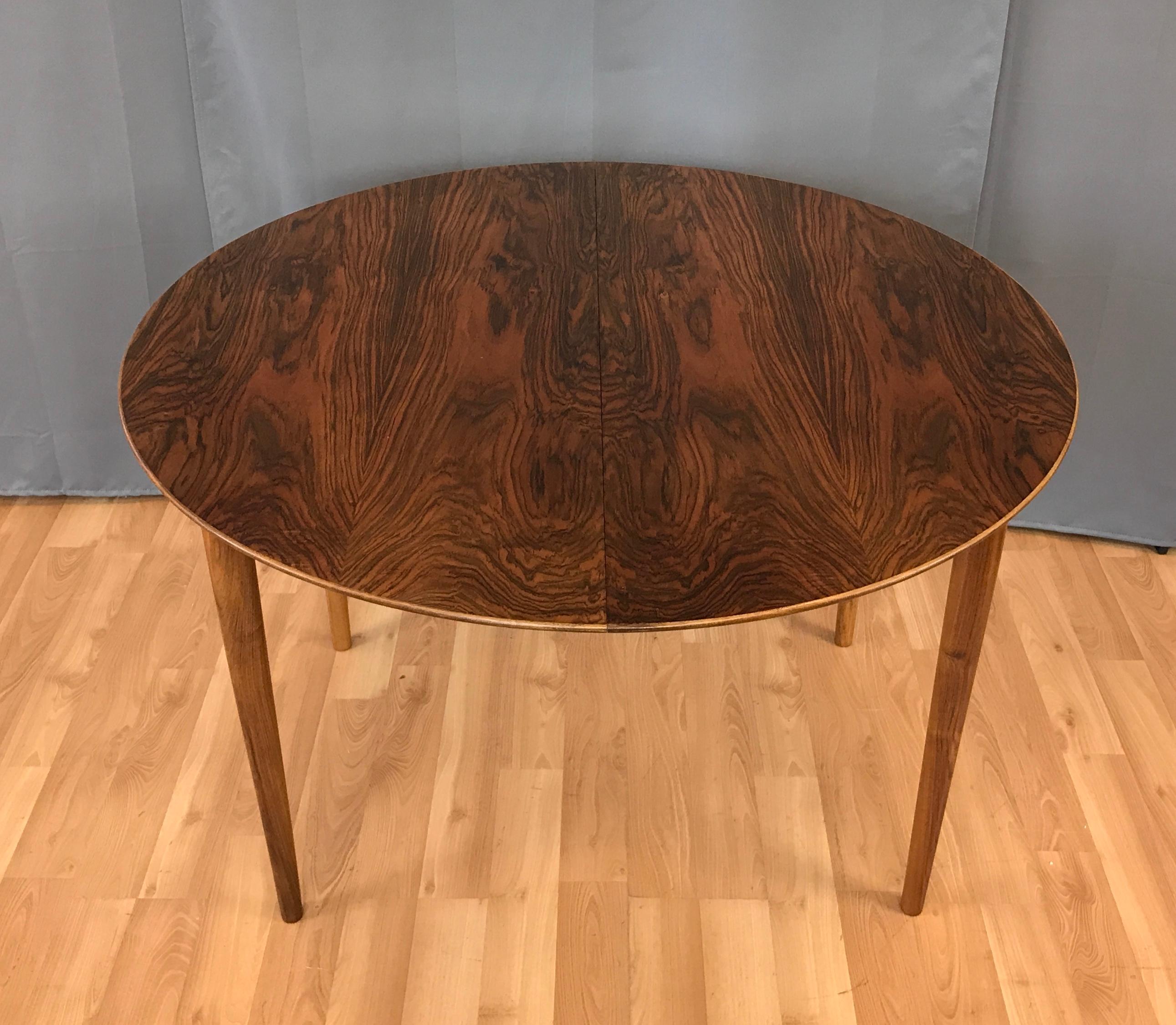 Danish modern round rosewood dining table by Kurt Ostervig. 

Table comes with one leaf that's 23.50 wide. When you put the one leaf in, it makes the table 68.75 inches wide. With the leaf in you can seat six. 

 