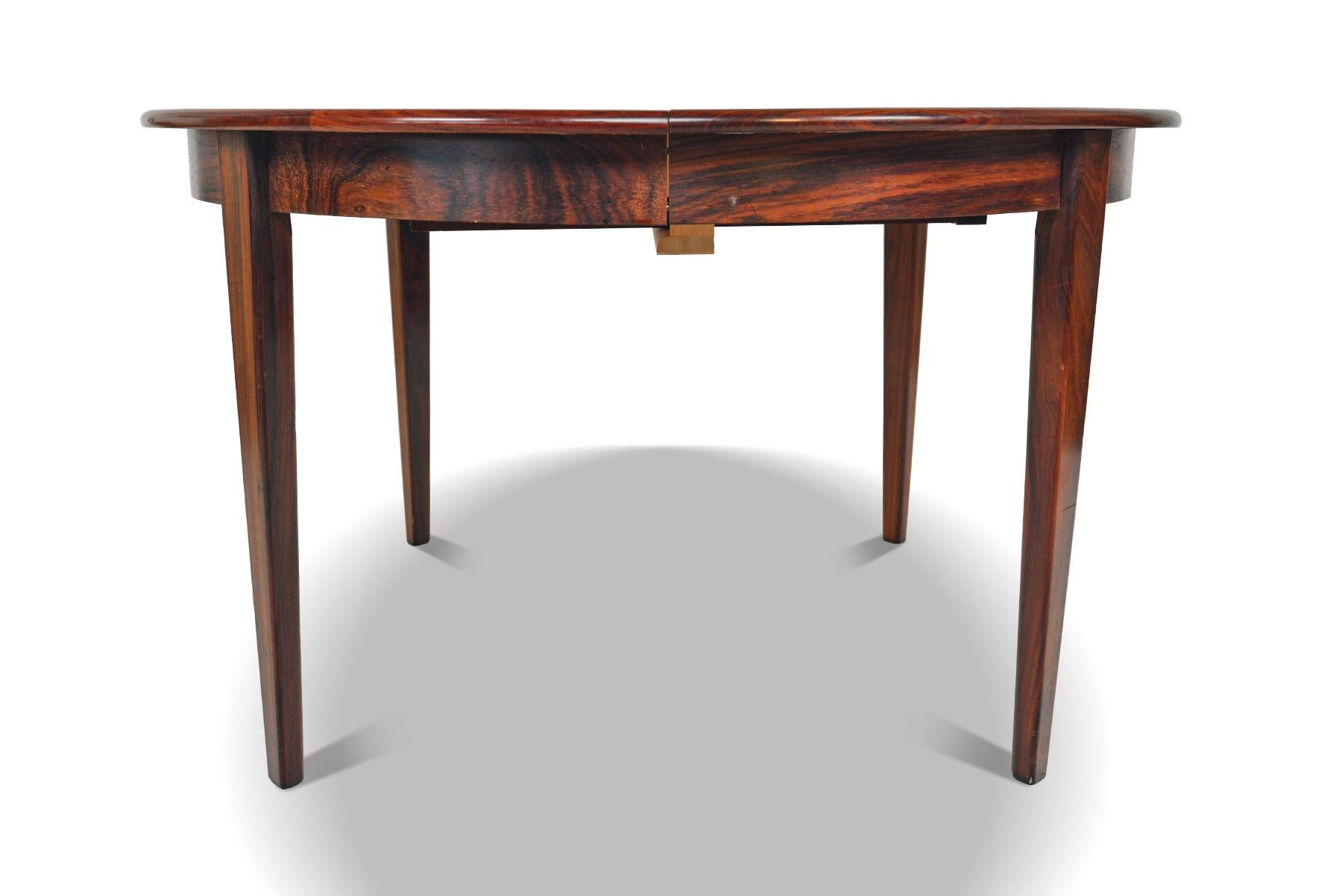 This beautifully elegant round dining table was manufactured by Moreddi in Denmark in the 1960s. Book- matched Brazilian rosewood wood grain is banded with a clean and simple line. Table extends to hold three additional leaves and can comfortably