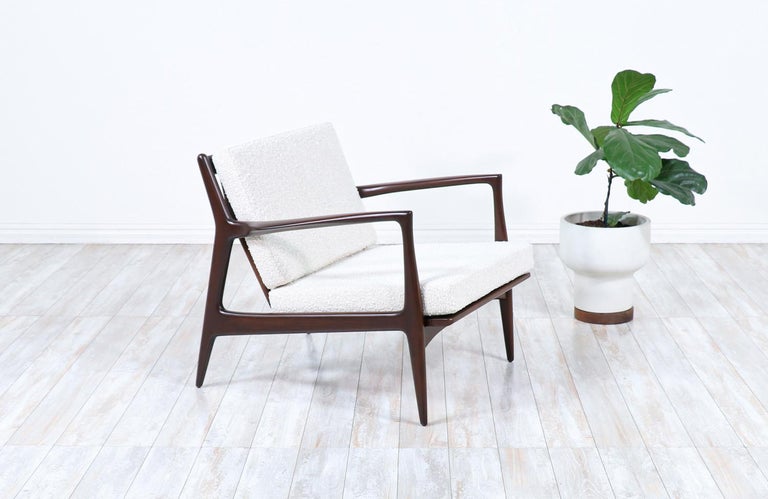 Stylish lounge chair designed by Ib Kofod-Larsen for Selig in Denmark circa 1960s. This sleek and ergonomic lounge chair features a sturdy wood frame with angled legs and a sculptural slatted back that is held in place by a bowed perpendicular