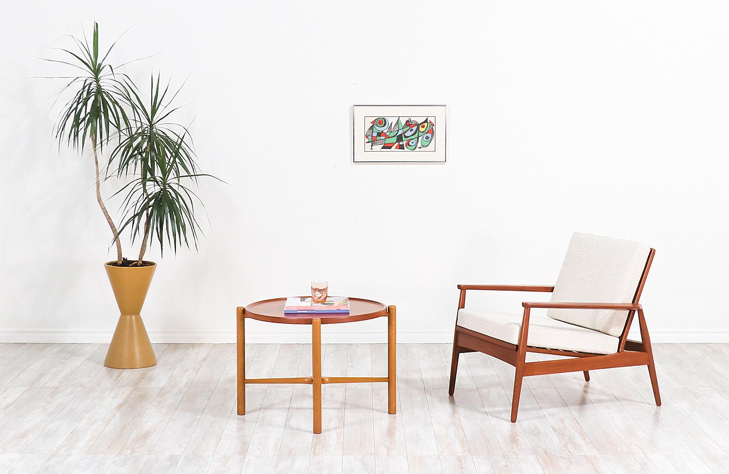 Stylish Danish modern lounge chair designed and manufactured in Denmark, circa 1950s. This elegant chair features a solid teak wood frame with an organic design, curvilinear armrests, and a slatted backrest for a clean aesthetic. The removable