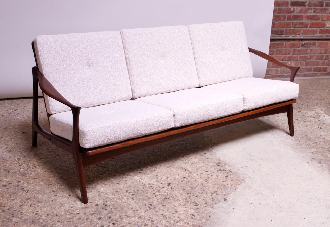 Danish modern sofa composed of a rosewood frame with beechwood inlay detail to the arms. Slat-back construction with deeply sculpted arms. Sharp lines and elegant form. Single button tuft to back and seat cushions.
Rosewood has been newly
