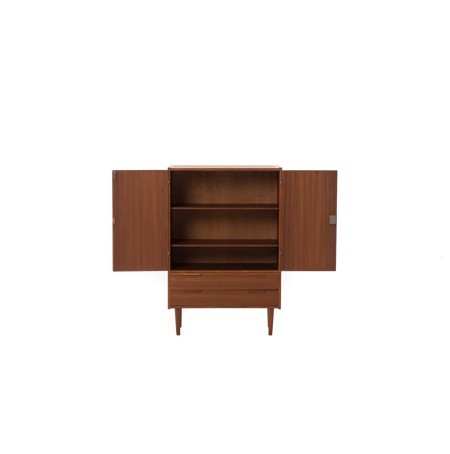 Danish modern upright teak cabinet. This versatile design could work in a variety of settings. Cupboard with locking doors adjustable shelves, two storage drawers underneath.