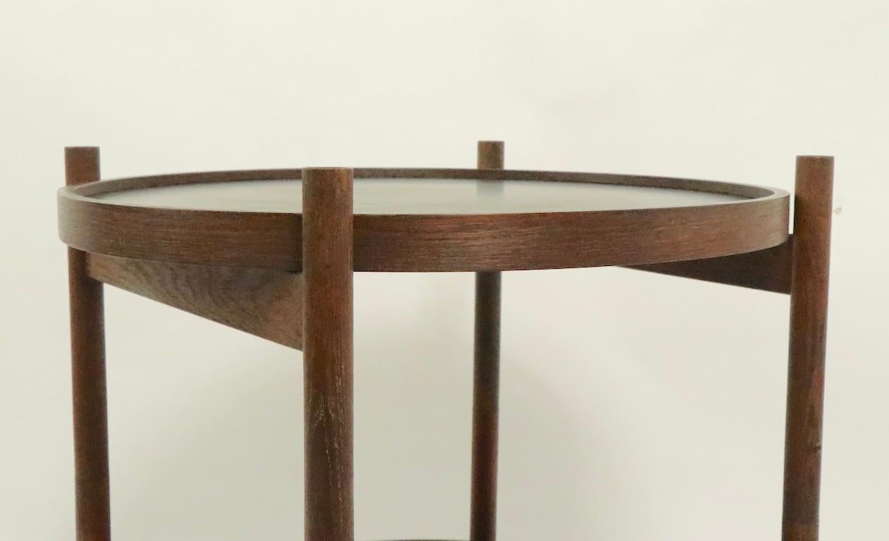 Rare Danish modern serving cart having two disk form removable trays, each with a red surface, and a black surface. The frame is solid teak, and folds to flat for easy moving and storage. The trays have laminate surfaces, each tray shows some