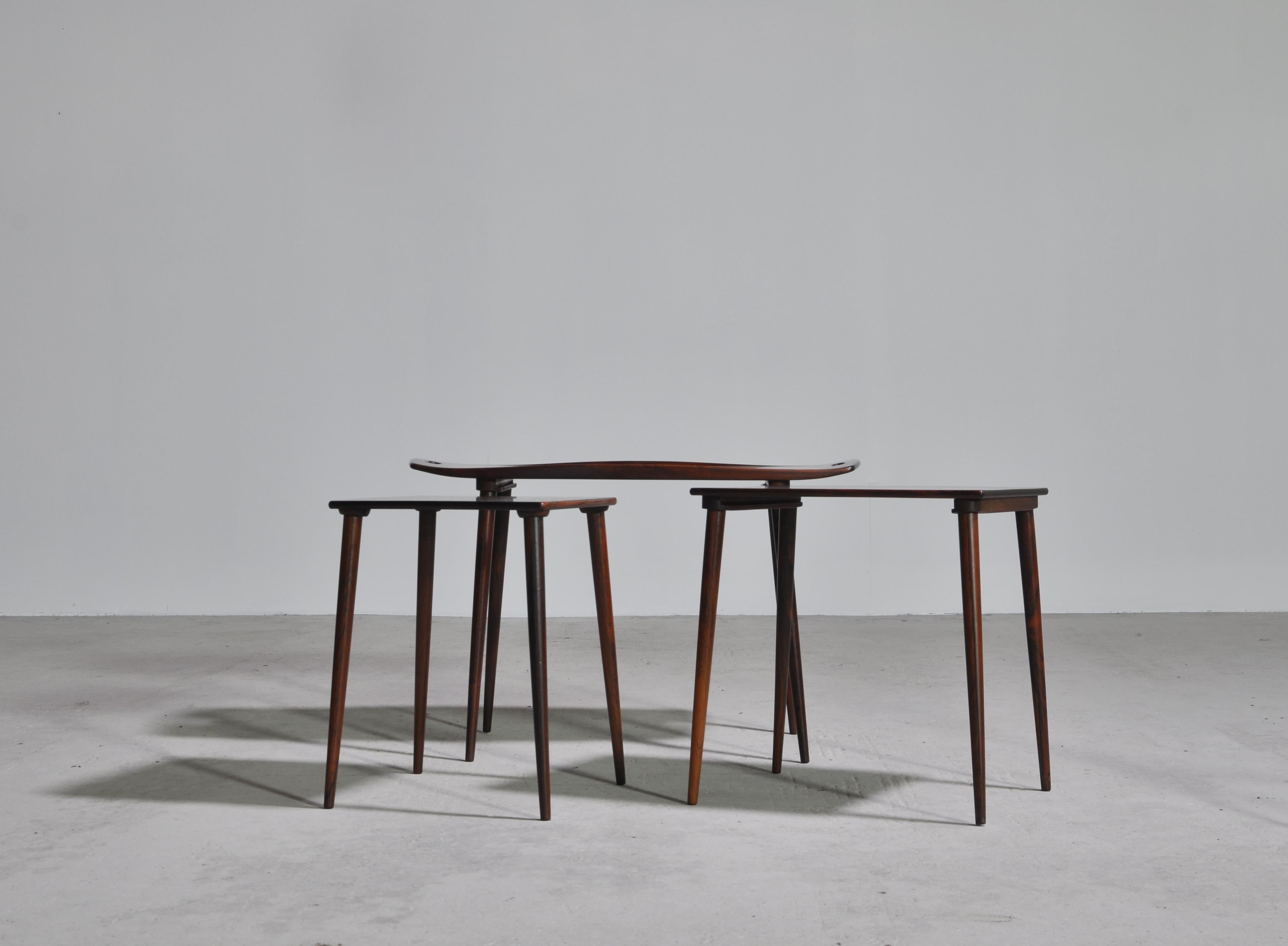 Highly detailed and beautiful rosewood nesting tables with serving tray handles designed by Jens Quistgaard for Richard Nissen. The sculpted top of the largest table features finger cut-outs at each end, raised edges and slender, tapered legs. A