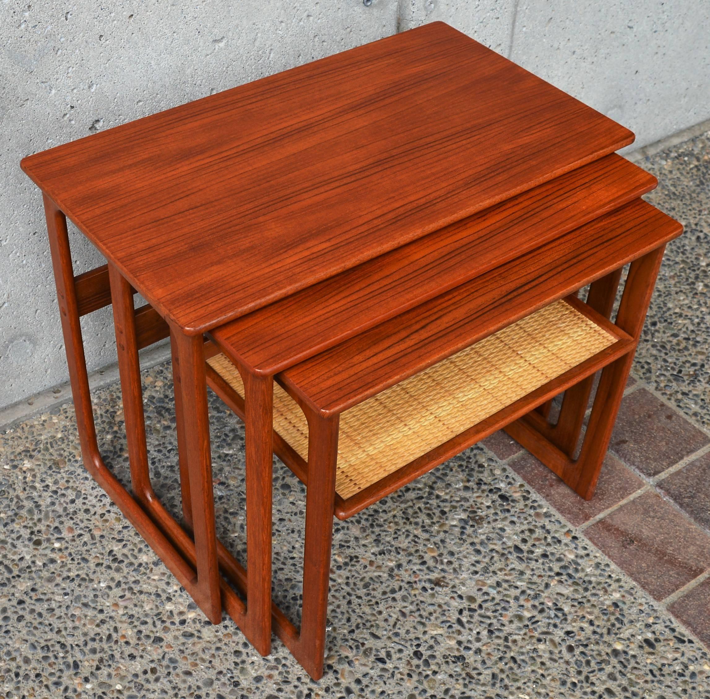 This gorgeous set of three Danish modern teak nesting tables are larger than typical, have rectangular closed sides with oval cut-always on the inside. Well constructed, the lower one has a delightful woven cane shelf. A striking set that looks