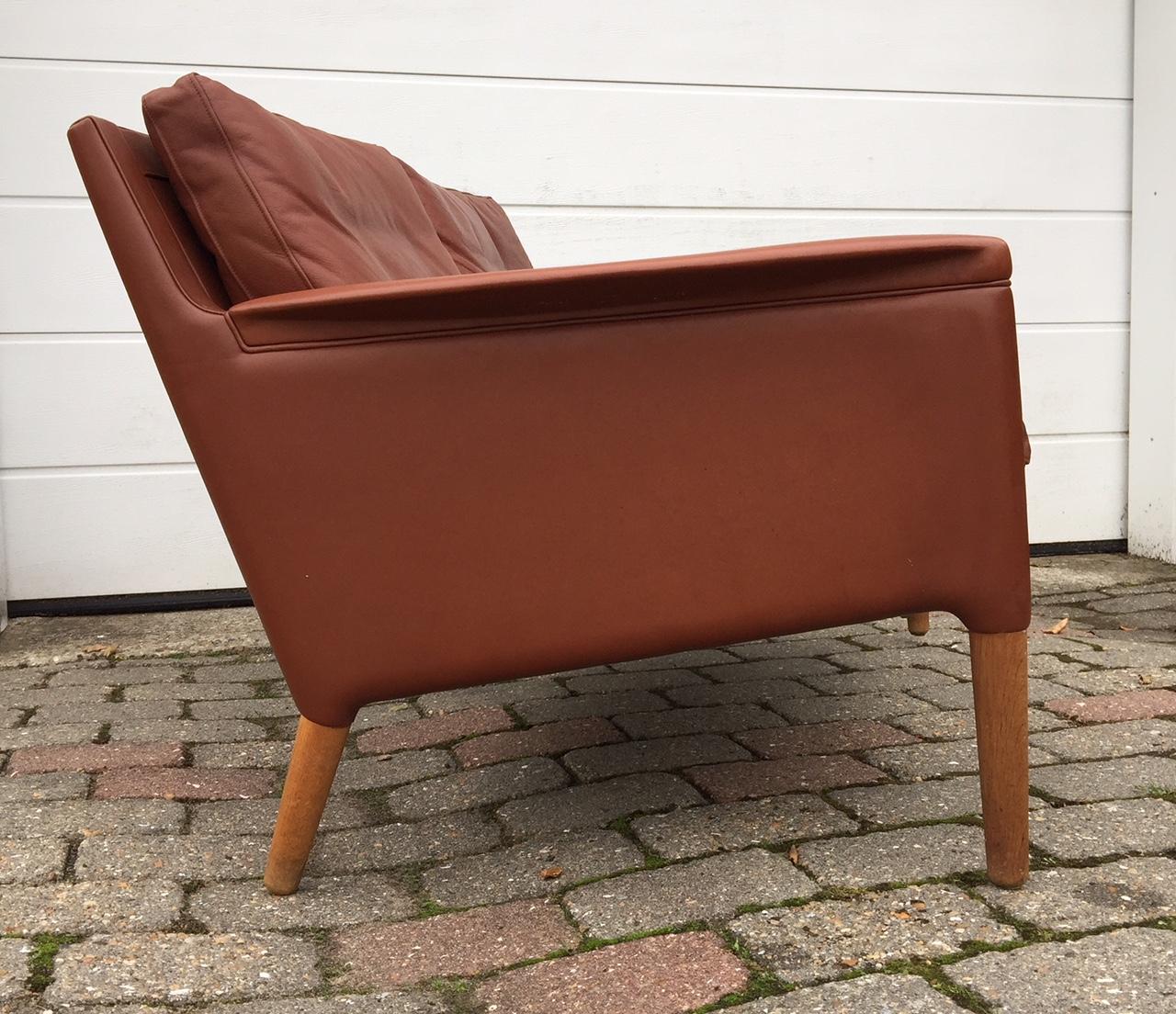 Kurt Ostervig designed tanned leather two-seated sofa or Settee with tapered oak legs. It features original upholstery and intricate leather upholstery details around the top part of the legs and to the armrests. It was manufactured by Centrum