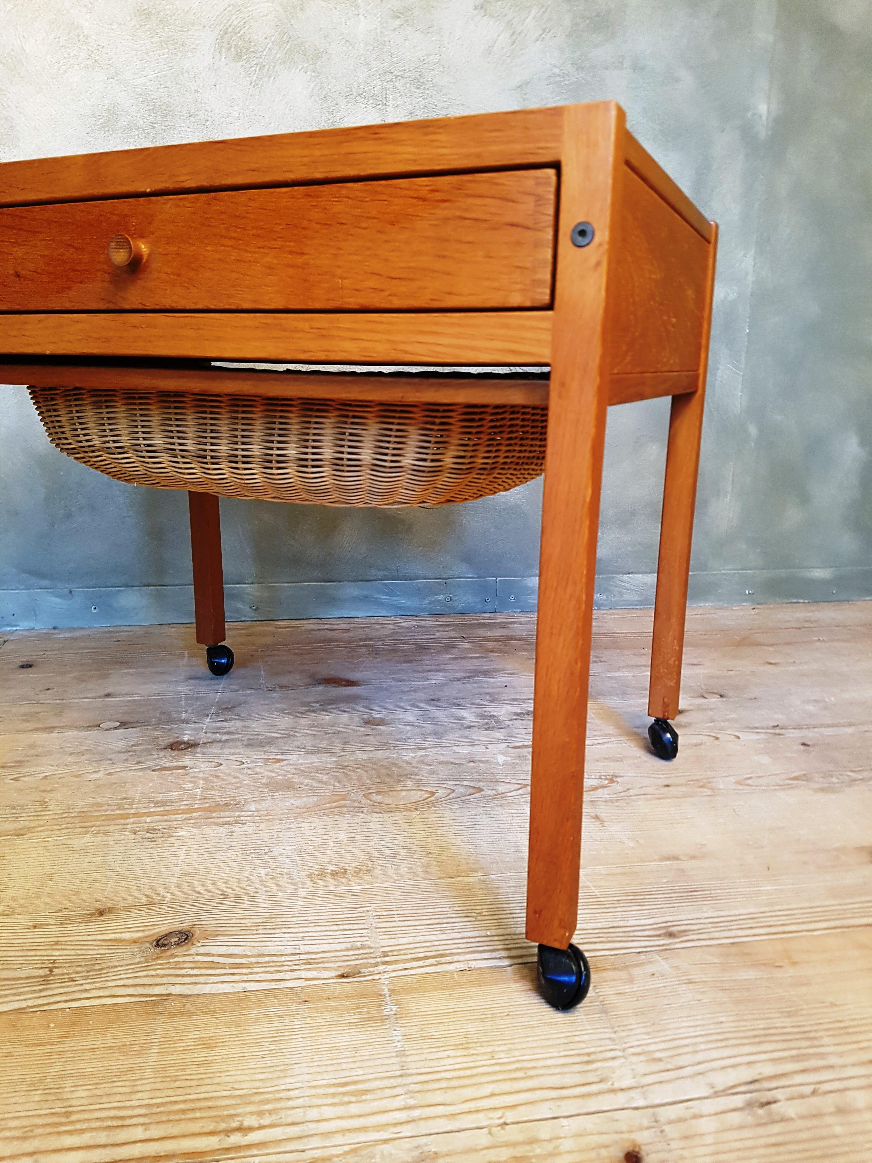 Sewing table or trolley with large drawer and pull-out rattan basket on wheels. A piece of craftsmanship in the Danish Modern style of the 1960s. Despite its size, the table looks light and delicate. The model is reminiscent of the sewing table by