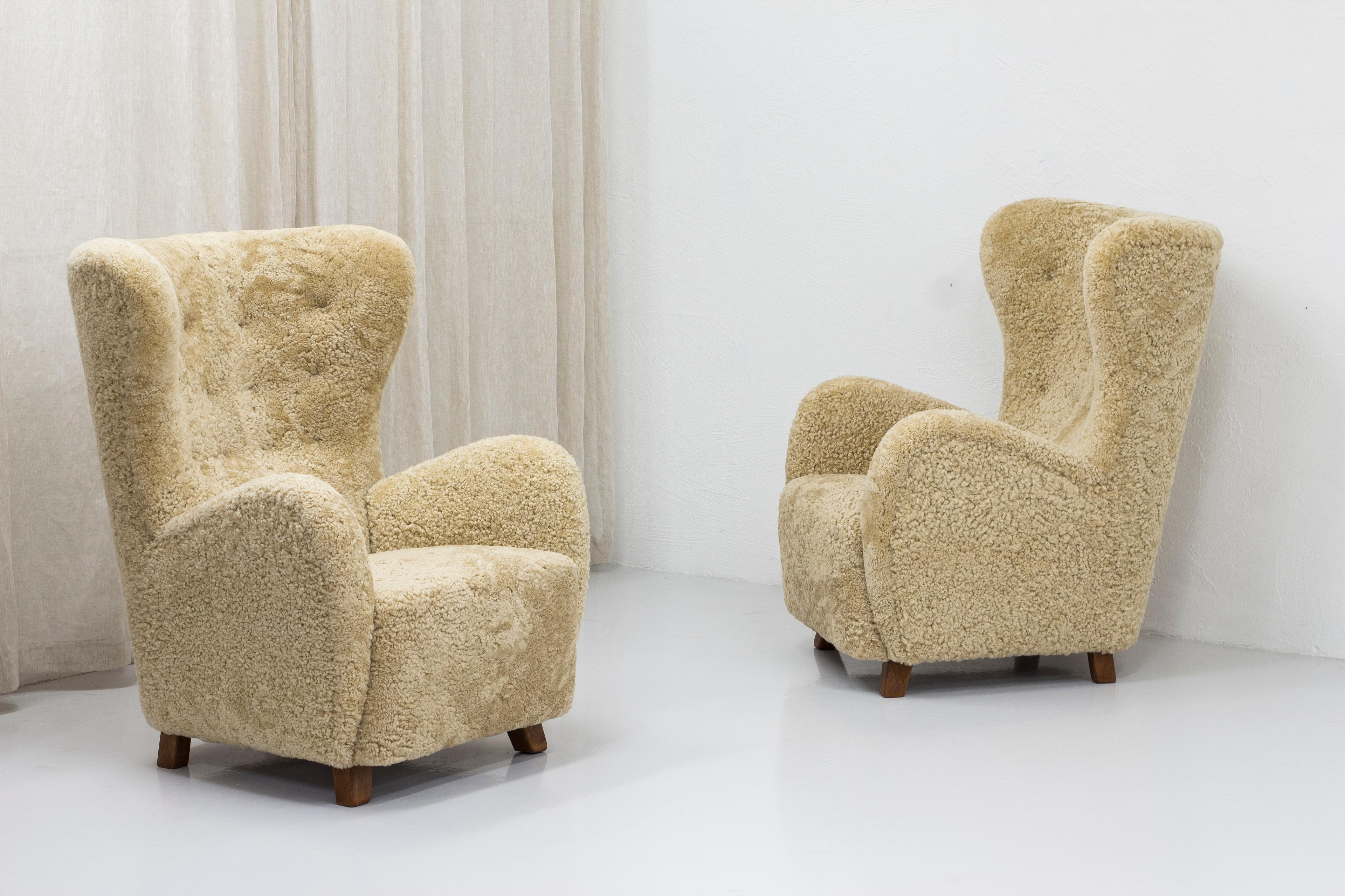 Pair of large Danish modern high back lounge chairs. Designed and made in Denmark during the 1940-50s. Large and highly comfortable. The chairs have been reupholstered in high quality sheep skin in a light beige/blonde color. The legs have been