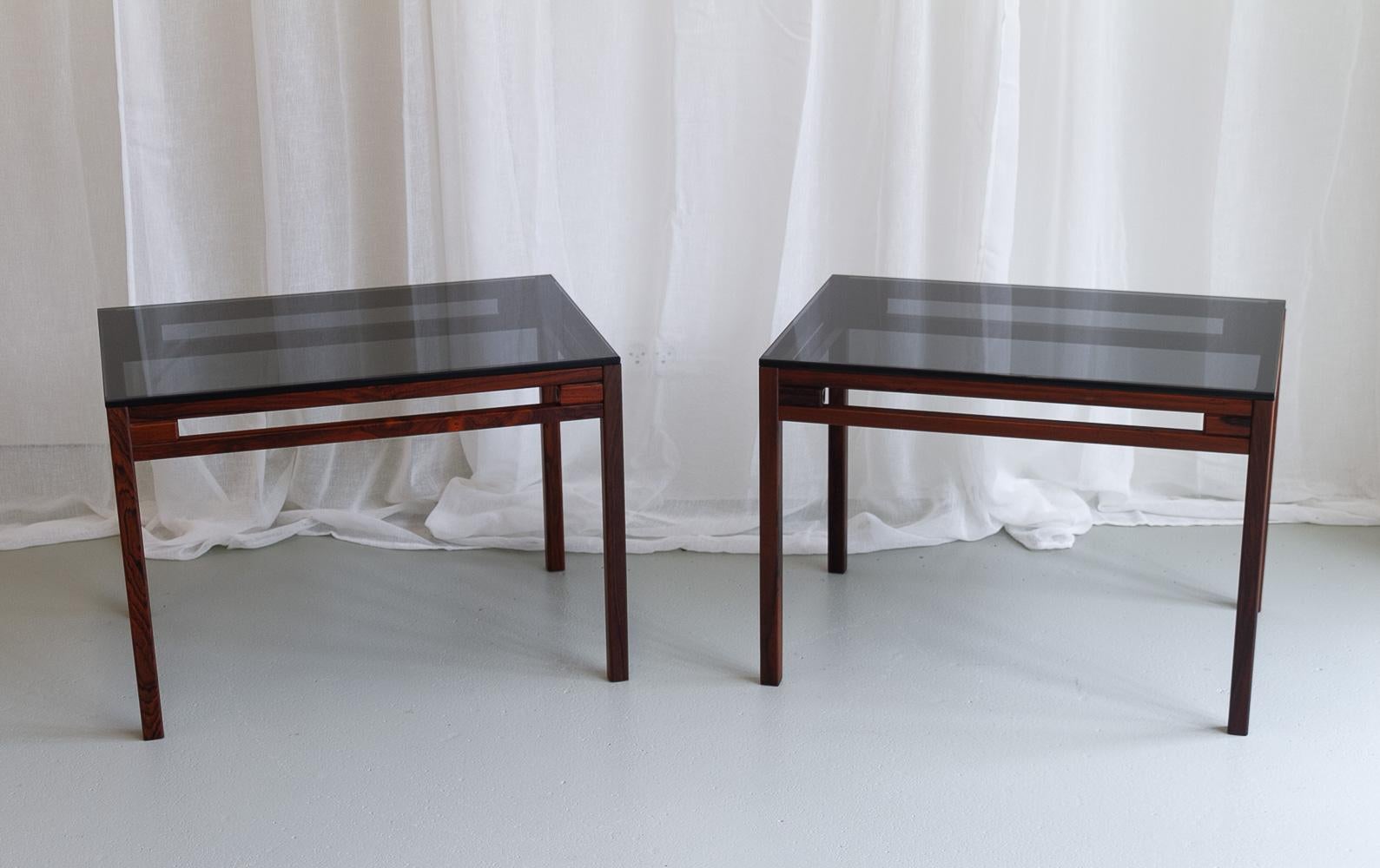 Danish Modern Side Tables in Rosewood and Glass, 1960s. Set of 2.
Elegant and stylish pair of Danish Mid-Century modern sidetables made in Denmark in the early 1960s. Frame in solid rosewood/palisander and table tops in smoked glass.
Suitable for