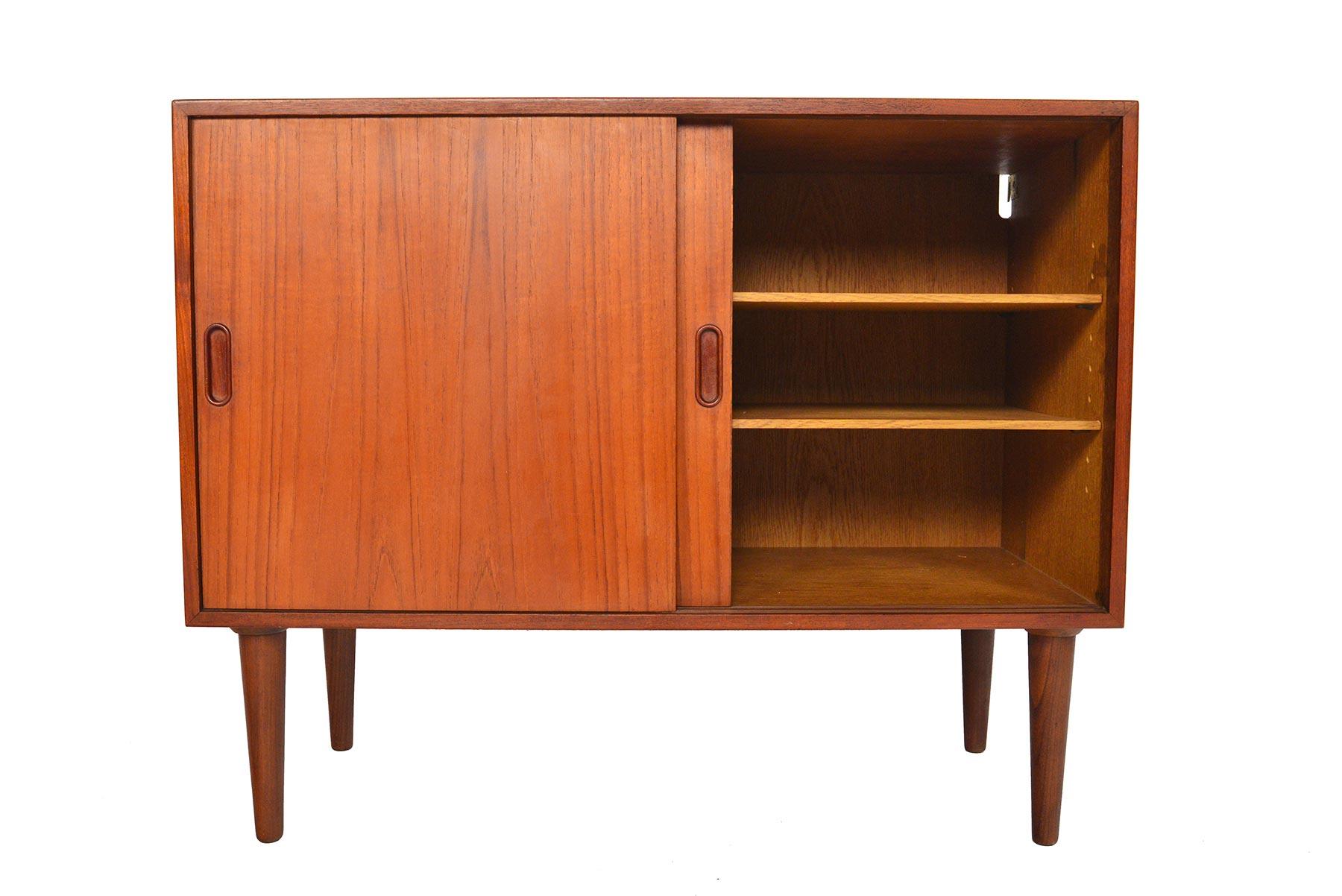 This small Danish modern midcentury credenza is the perfect storage solution for any modern home. Crafted in teak, this piece features two sliding doors which open to an oak lined interior offering two bays and adjustable shelves. Piece stands on