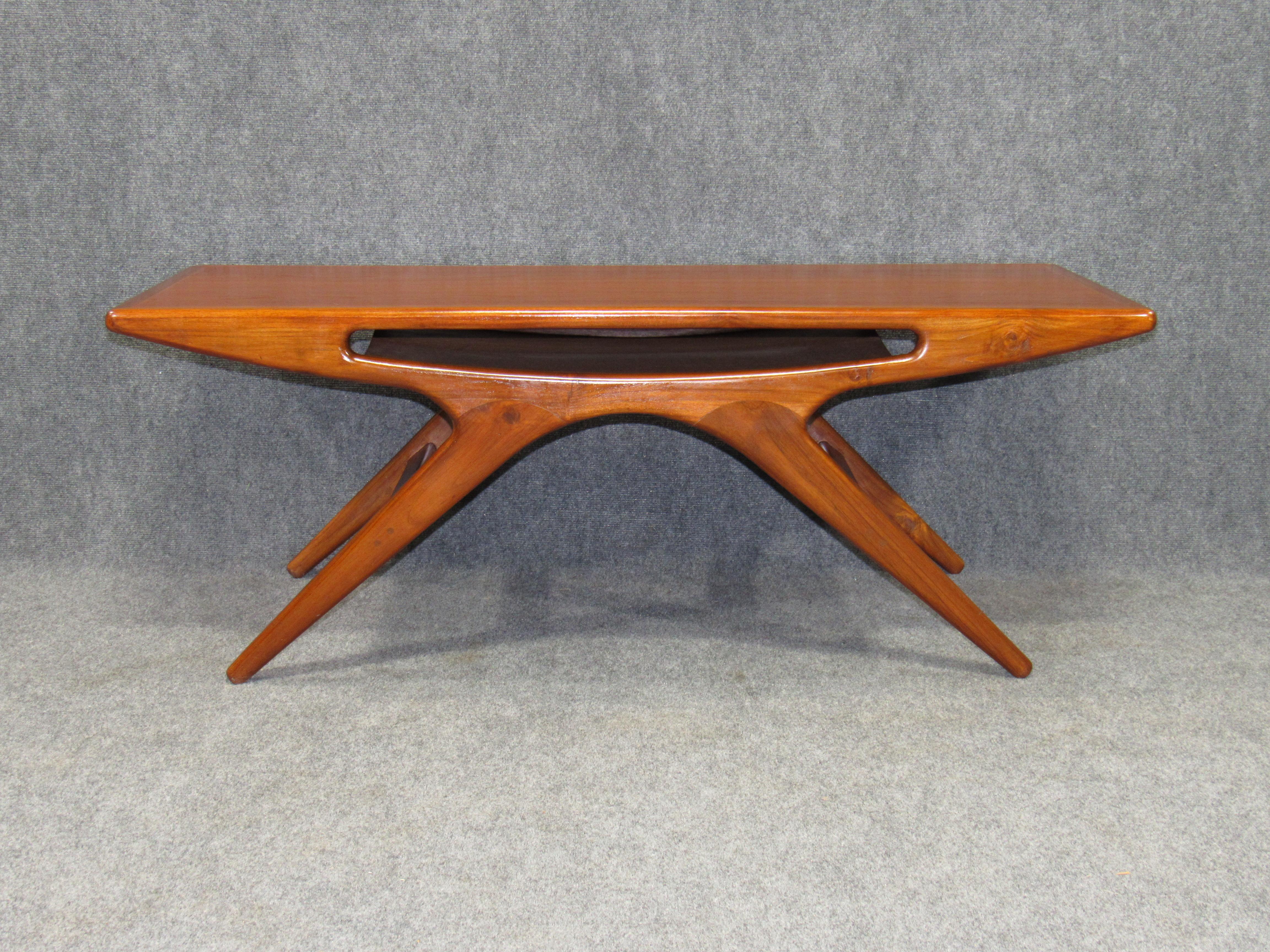 A triumph of Johannes Andersen's design prowess - the smile coffee table - is a rare and collectible piece. The design succeeds as being functional as well as playful and elegant. It has a sleek teak body with a center pocket shelf.