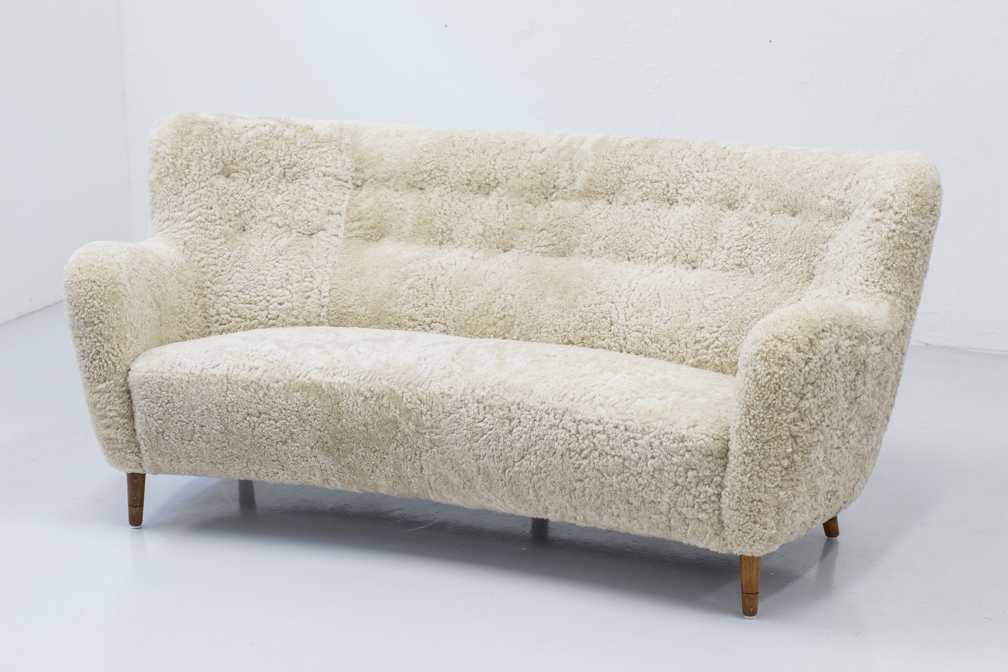 Danish modern sofa in the manner of Finn Juhl. Reupholstered with creme colored sheep skin. Slightly tapered legs in solid beech wood. Beautiful shape with a slight curve. Tufted back rest with brown leather buttons. The upholstery is new and the