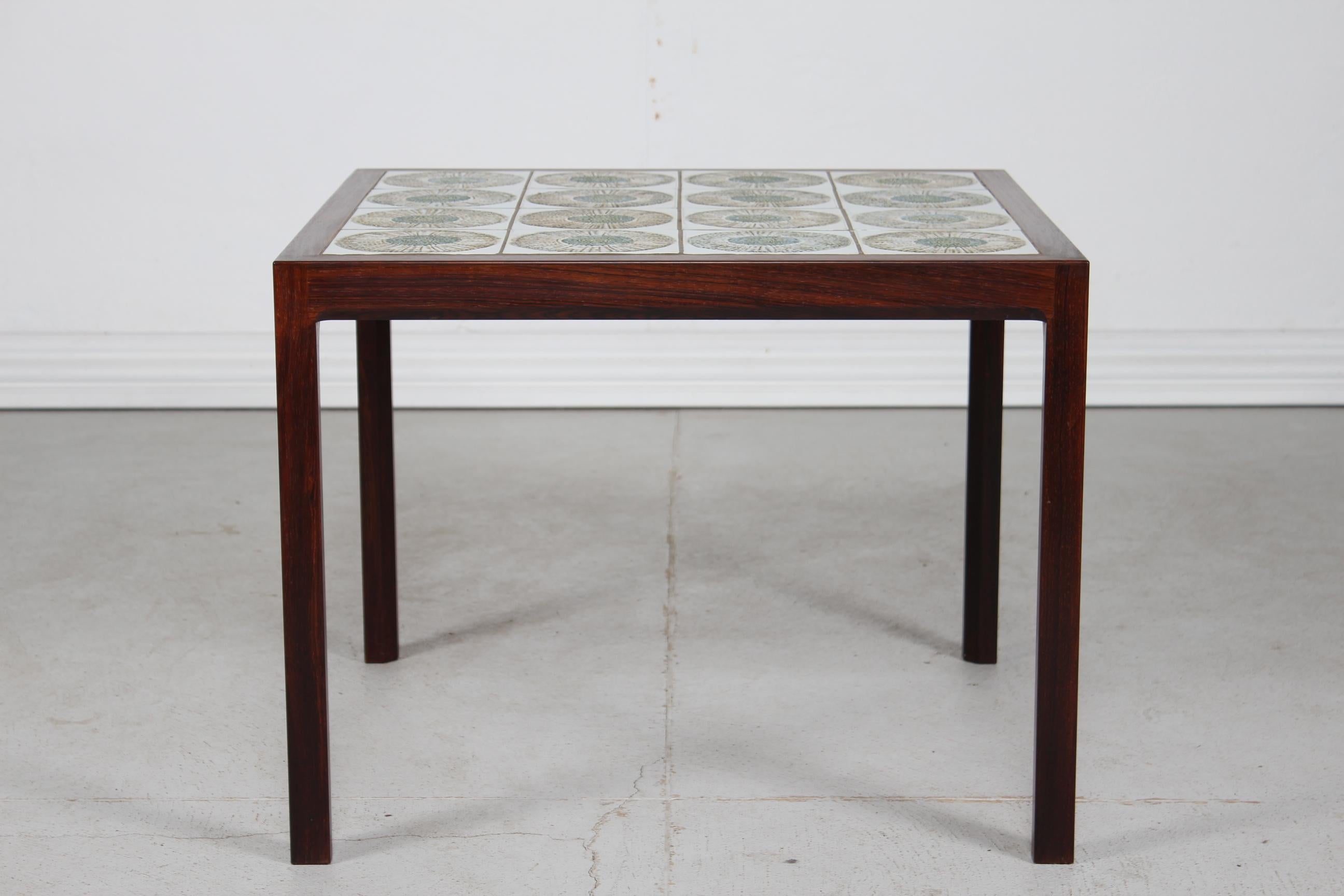 Midcentury Danish coffee table with dark wood veneer and inlaid ceramic tiles from Royal Copenhagen. Made in the 1960s.

The tiles are designed by Kari Christensen and show an abstract flower blossom decor in white, blue and brown colors. They have