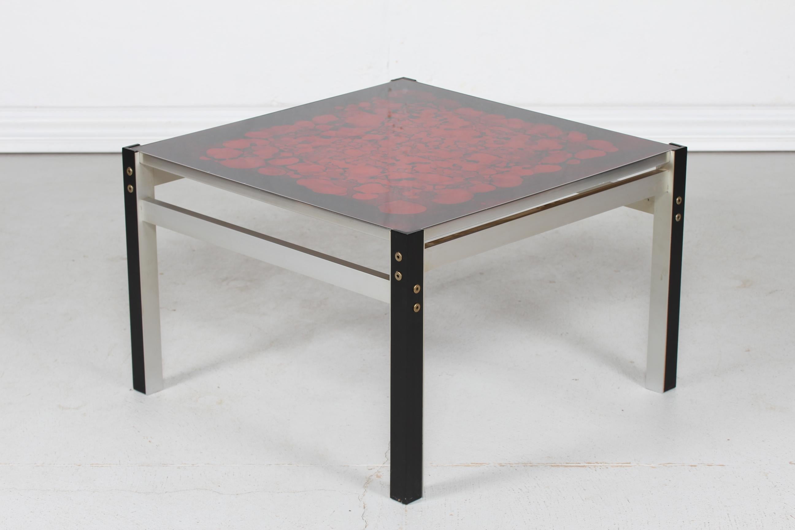 Danish modern square coffee table with red abstract decoration on the glass tabletop.
The frame and legs are made of aluminium.

A real typical 1970´s item.

Very nice vintage condition.
 