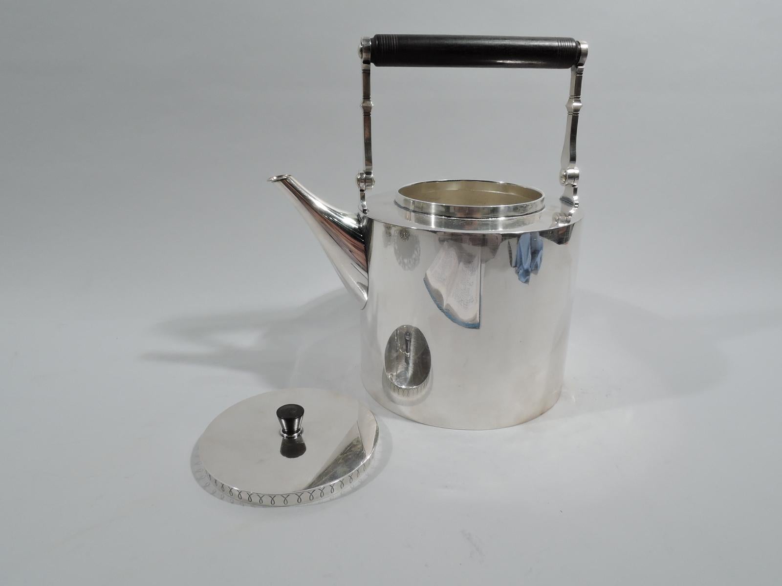 Mid-Century Modern sterling silver teapot. Made by Hans Hansen in Denmark in 1956. Drum-form with straight sides and tapering diagonal spout. Top flat. Cover same and inset with tapering stained-wood finial; cover sides have tooled interlaced arcade