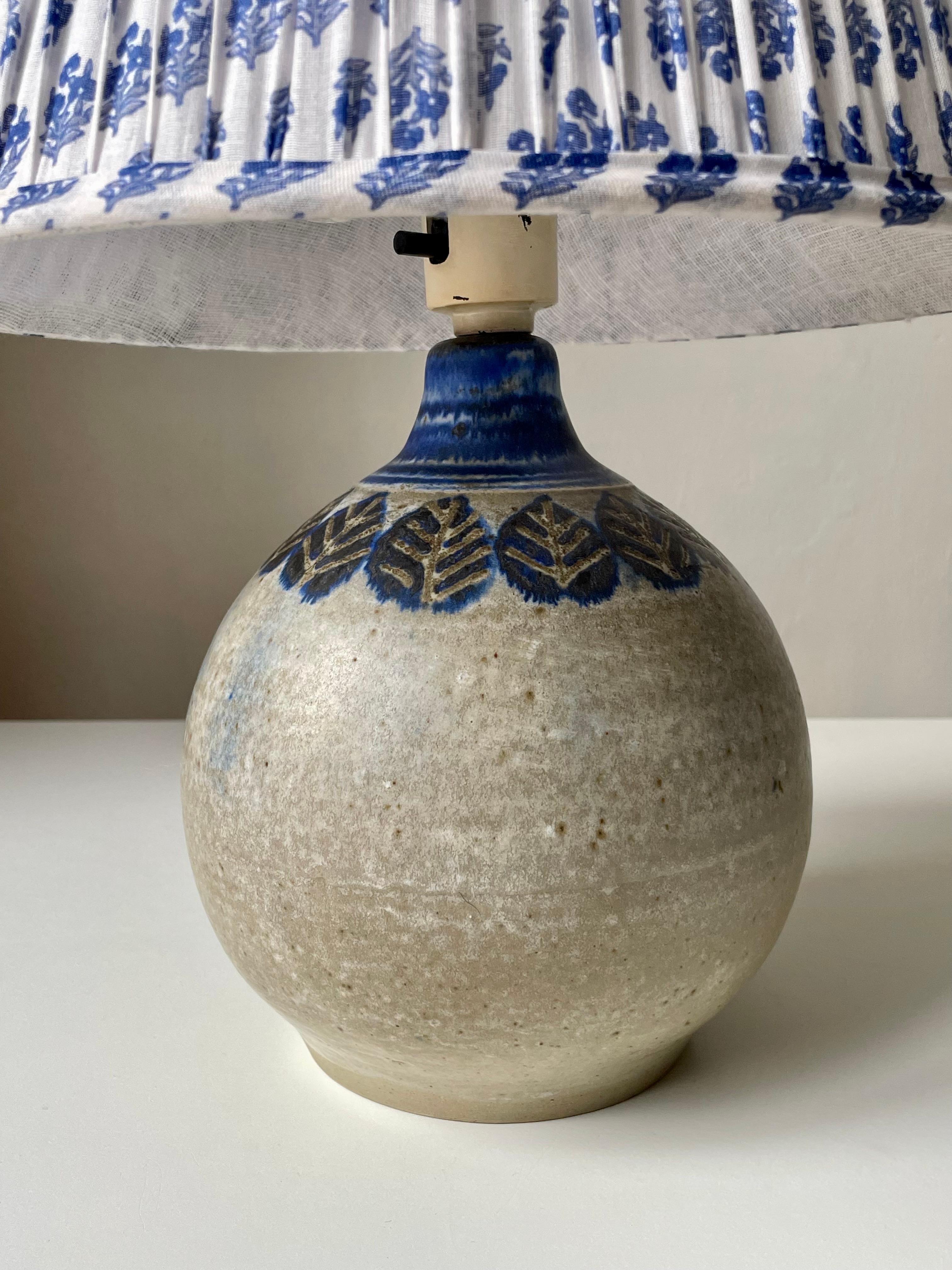 Lampe de table circulaire en céramique moderne danoise émaillée de couleur sable avec des feuilles stylisées bleues peintes à la main sous le col émaillé bleu. Conçu et fabriqué à la main par Nis Stougaard sur l'île danoise de Bornholm dans les