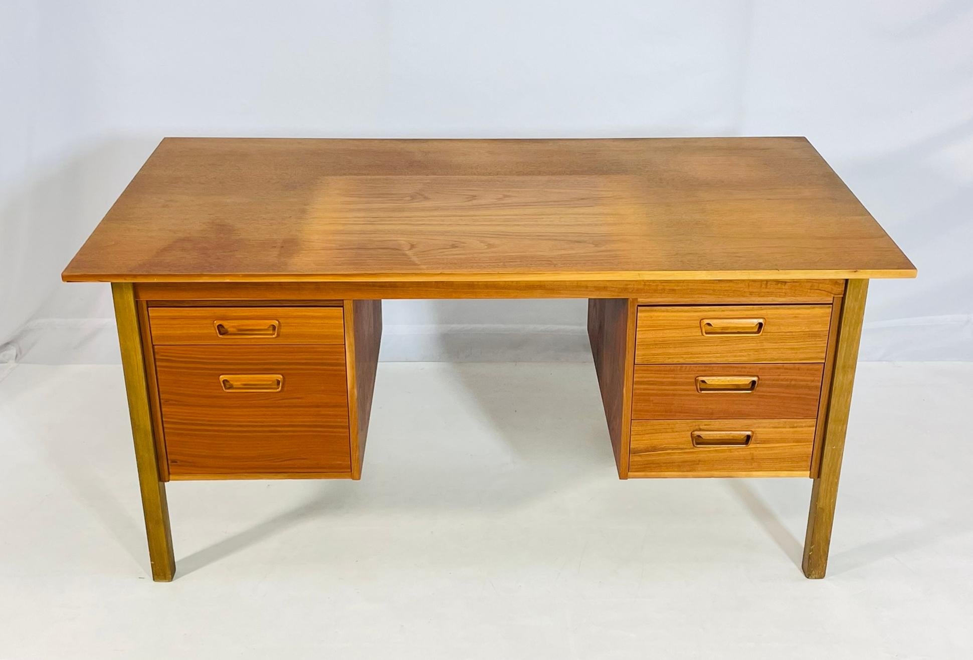 A beautifully proportioned Danish executive desk from the 1960s, crafted in richly figured teak with warm brass-toned accents. This striking piece features a spacious rectangular top over dual pedestal drawer configurations—three graduated drawers