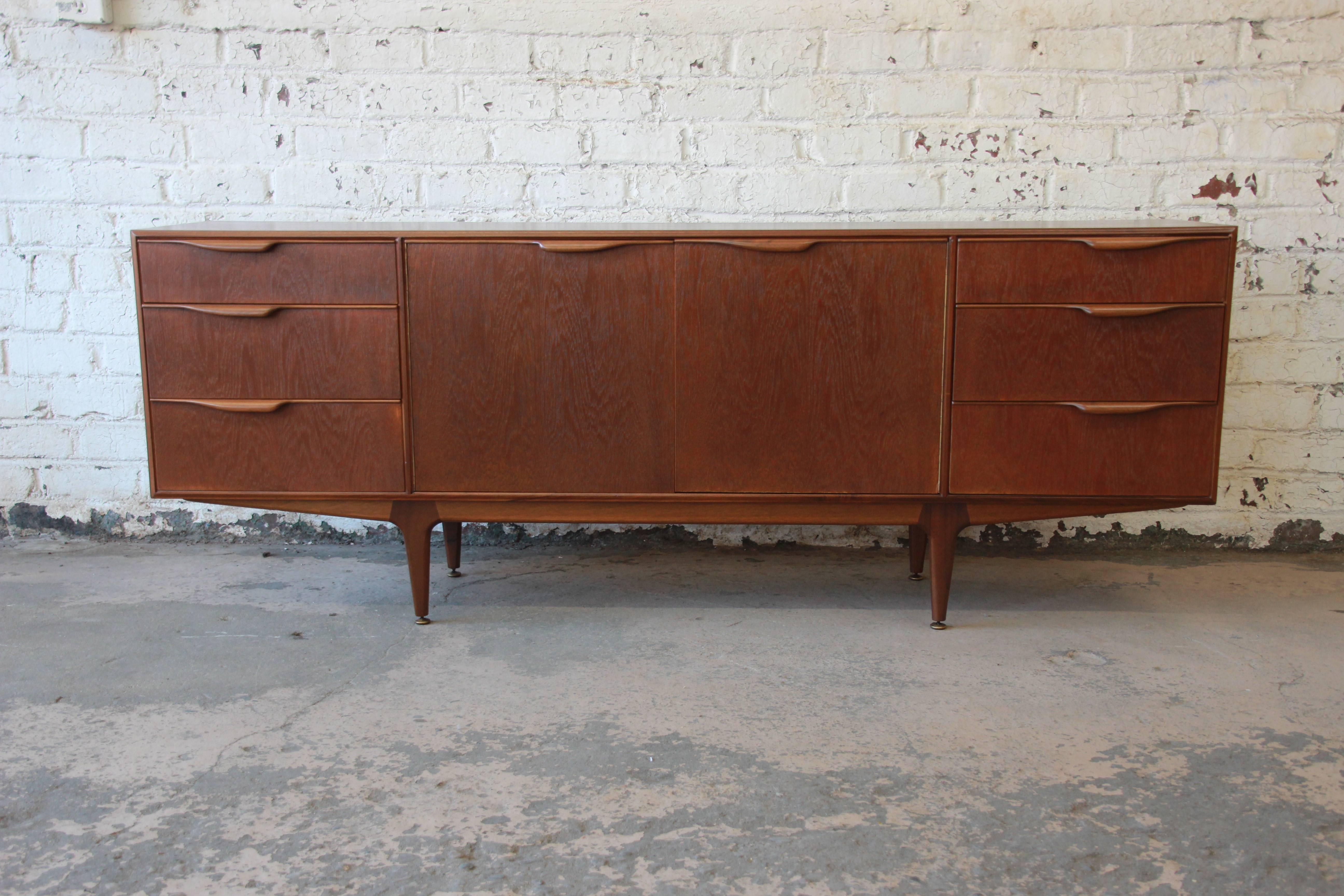 Offering a newly refinished teak sideboard credenza by A.H. McIntosh. The sideboard has a nice symmetrical design with carved teak pulls on the drawers that flank the centre cabinet area. The cabinet doors open up to a shelf for storage and bottle