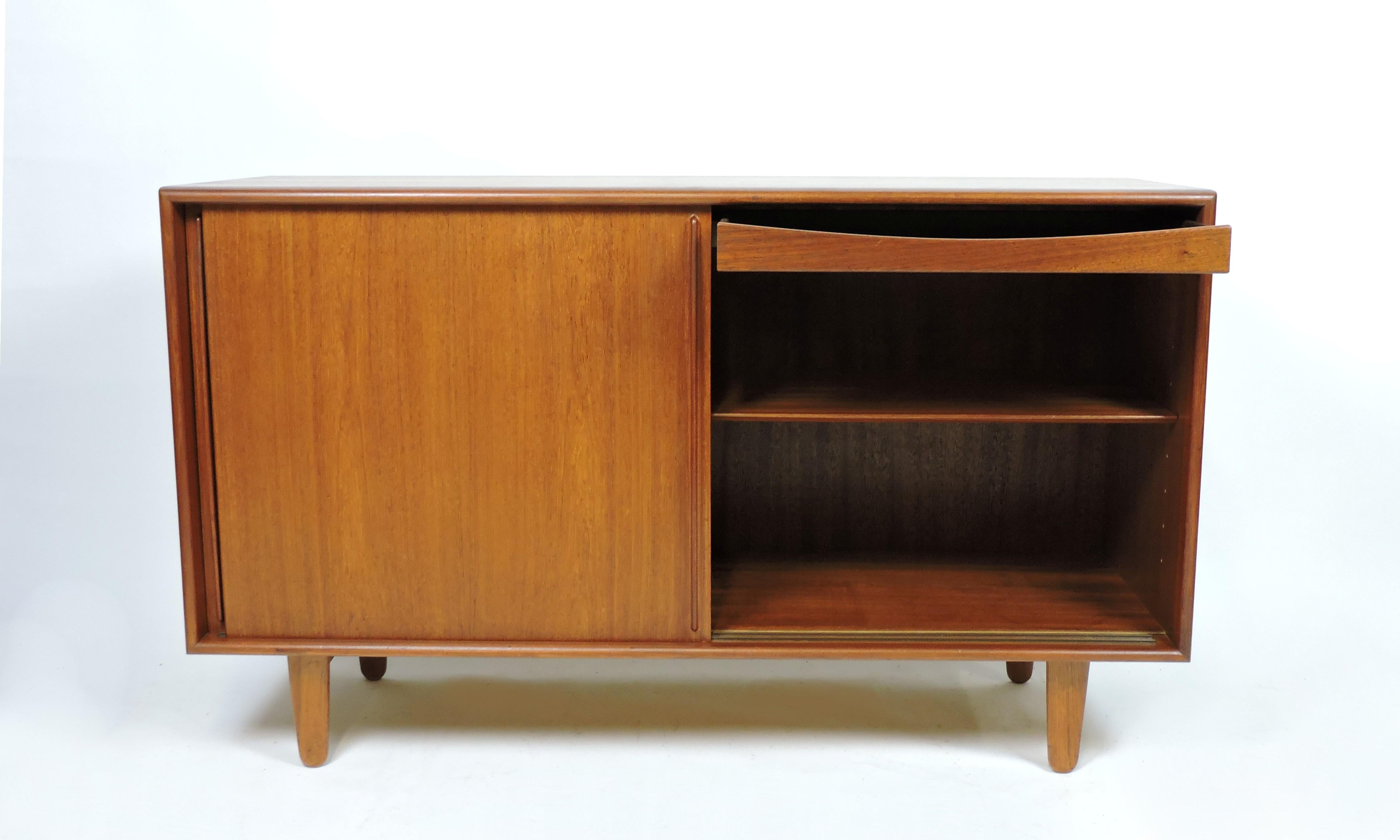 Beautiful Danish modern teak credenza designed by Svend Aage Madsen and made in Denmark by Falster Mobelfabrik. This cabinet has 2 sliding doors, behind which are 2 compartments with 3 adjustable shelves and a felt lined drawer for lots of storage