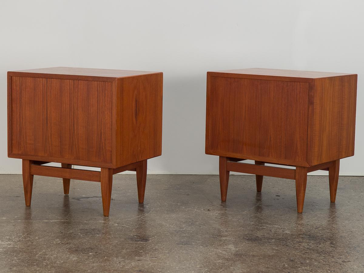 Pair of teak Scandinavian modern nightstands or end tables designed by Svend Madsen for Falster Denmark. Tambour doors slide smoothly to reveal an adjustable shelf and a pull out drawer. Cabinets are finished on all sides so that they may be floated