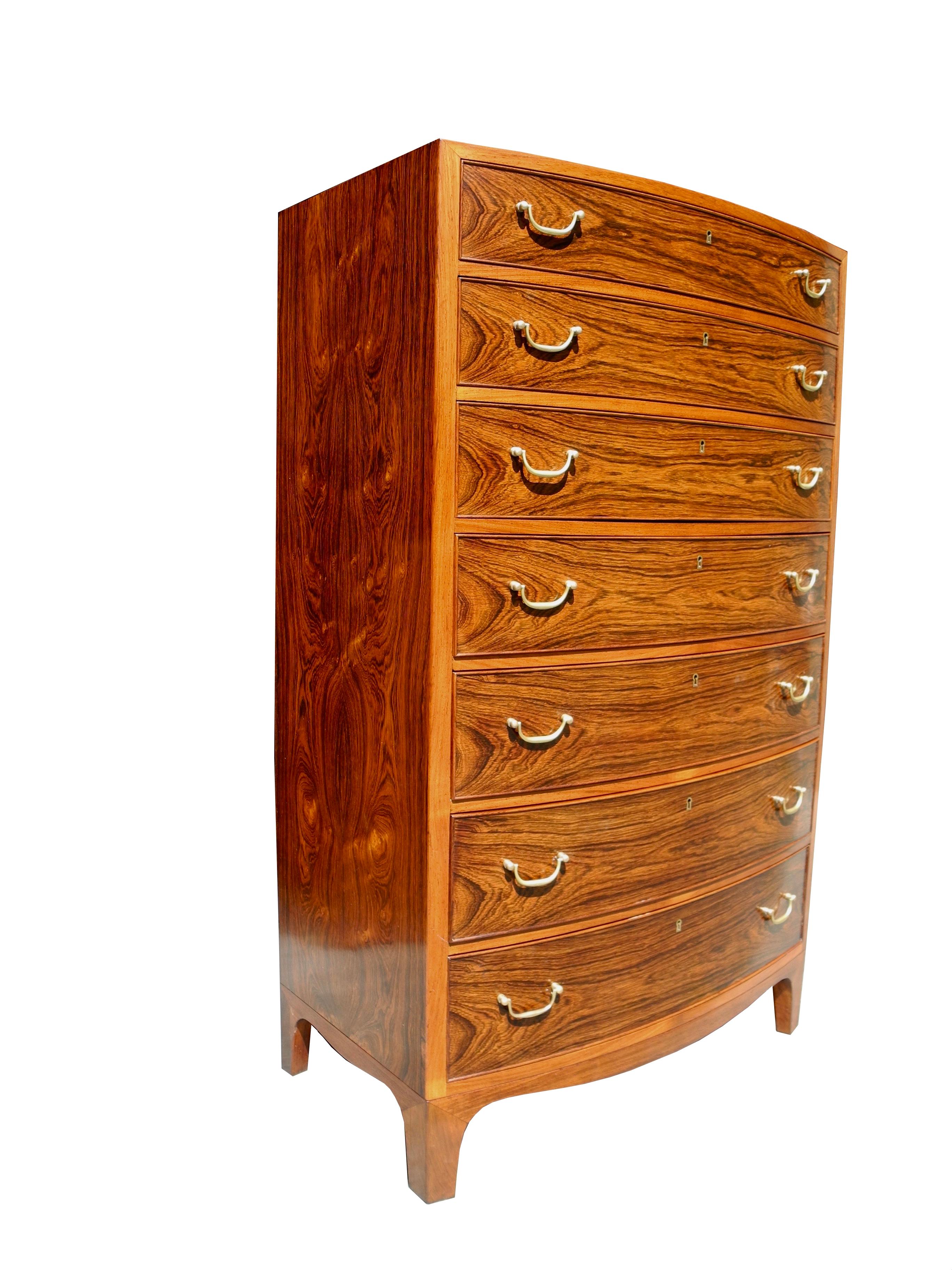 This beautifully crafted rosewood tall dresser with a subtle bombe front was made in Denmark and designed by the architect Ole Wanscher. Its condition is very good with clean insides, a refinished natural case and solid brass pulls.