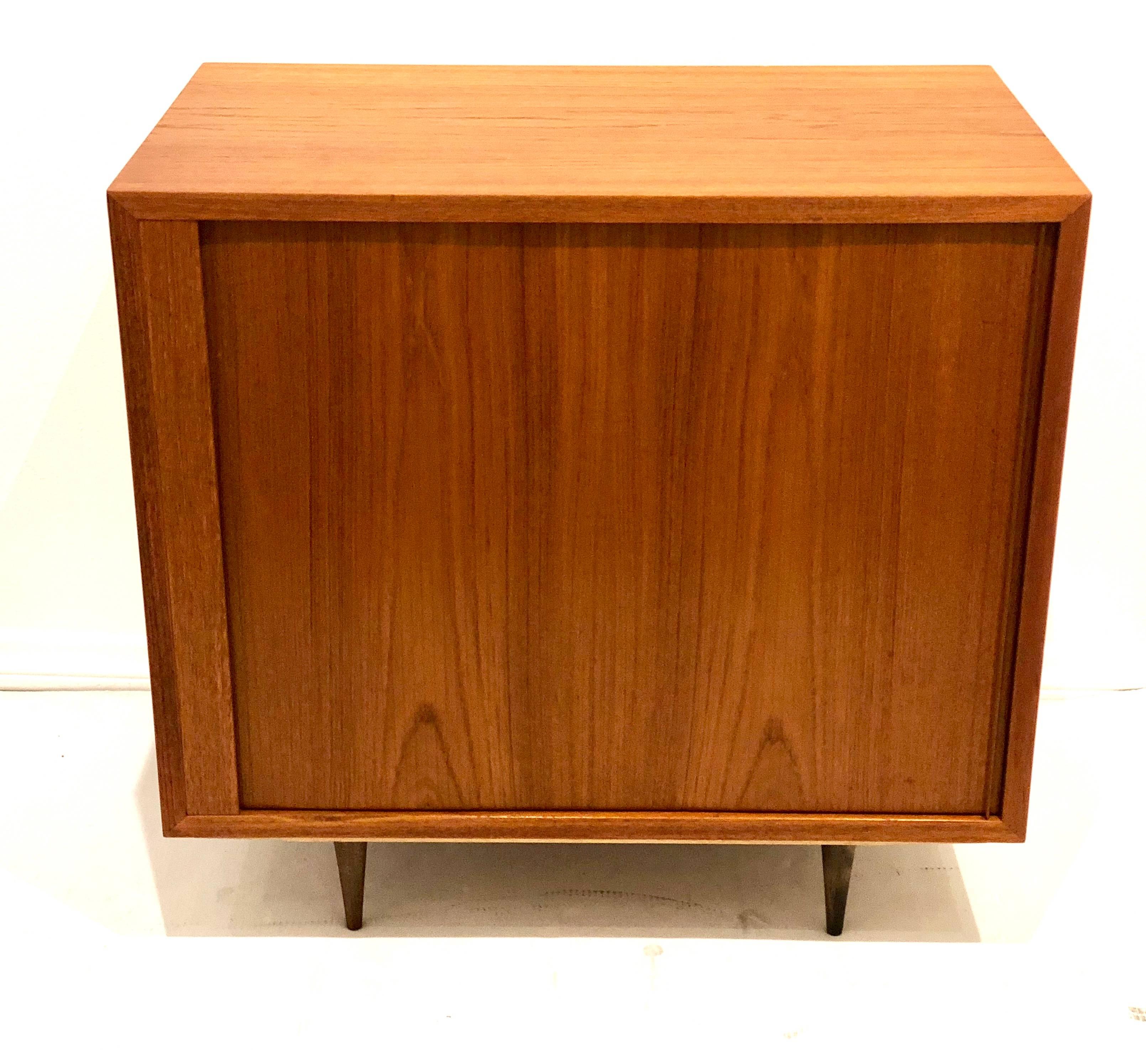 Versatile petite cabinet, circa 1950s Made in Denmark, tambour door that hides in one side freshly refinished, sitting on small tapered legs in walnut finish, design and manufactured by Paul Hundevad, retains its Danish control tag. With adjustable