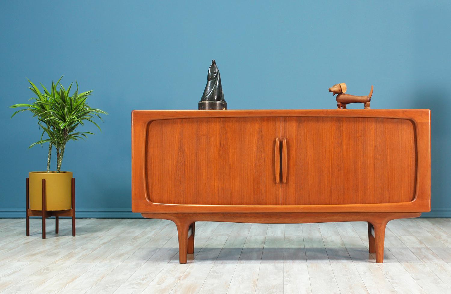 Elegant tambour door credenza designed and manufactured by Falster Møbelfabrik in Denmark circa 1950’s. This credenza features a spectacular teak wood frame with soft beveled inner edges and a solid teak wood base with subtly tapered legs supported