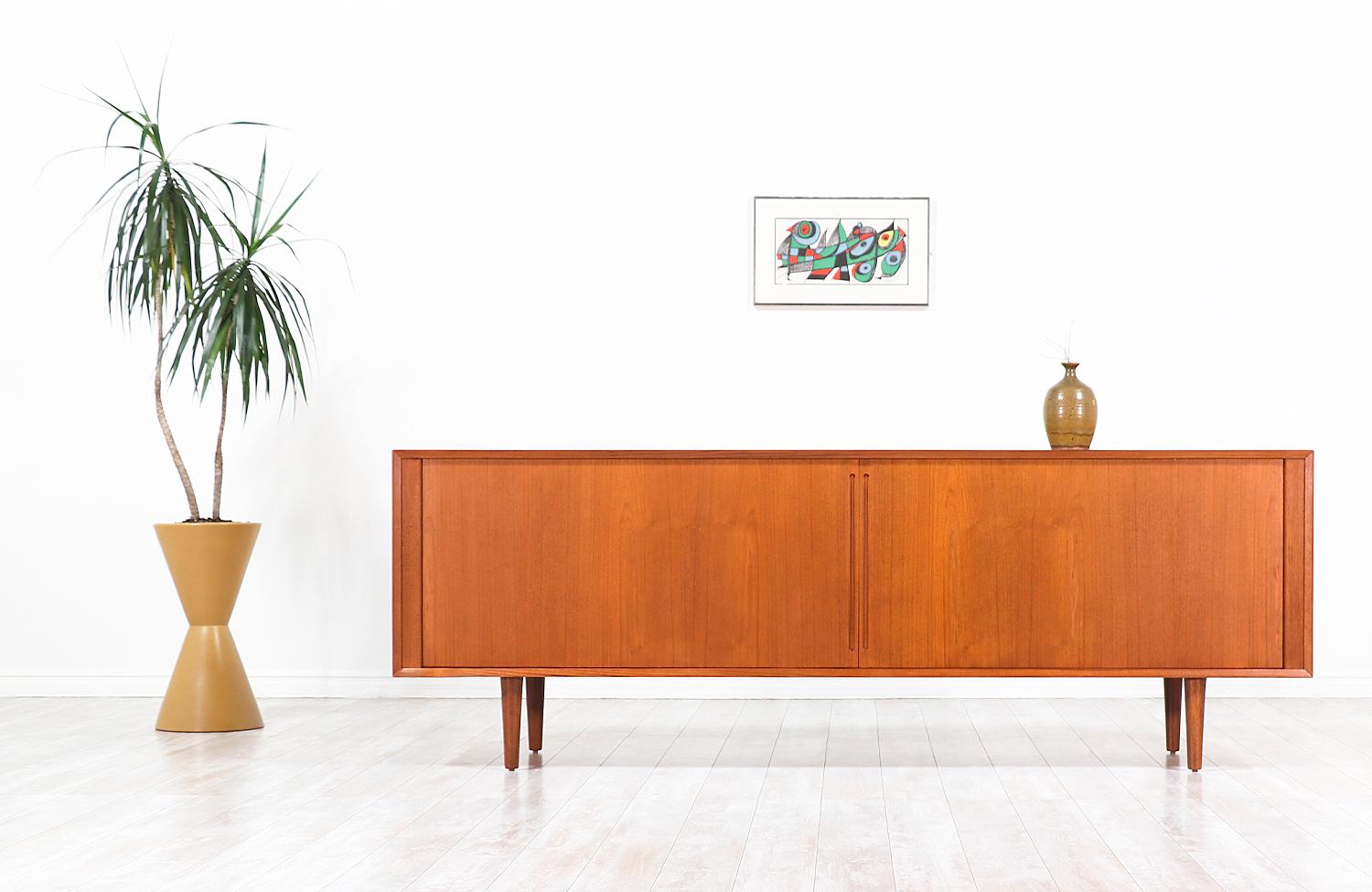 Minimalist modern credenza designed and manufactured in Denmark, circa 1960s. This long and low profile credenza features a teak wood construction with tambour doors and carved recessed handles. The doors slide smoothly on each side, revealing a