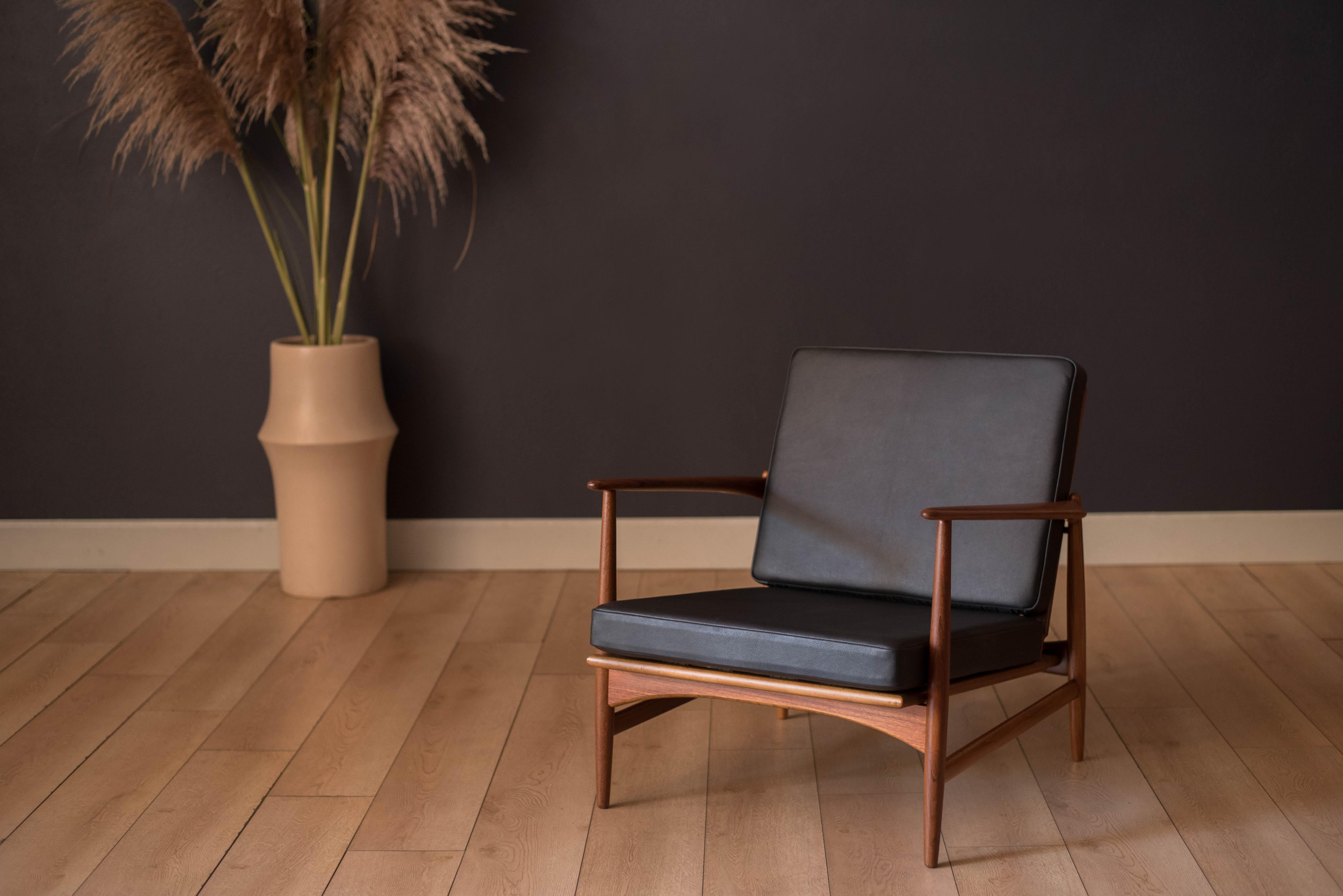 Mid-Century Modern lounge armchair in teak designed by Ib Kofod-Larsen for Selig, Denmark, circa 1960's. This vintage piece has been reupholstered in black leather with brand new foam and webbing. Features a sculptural teak frame with brass accents