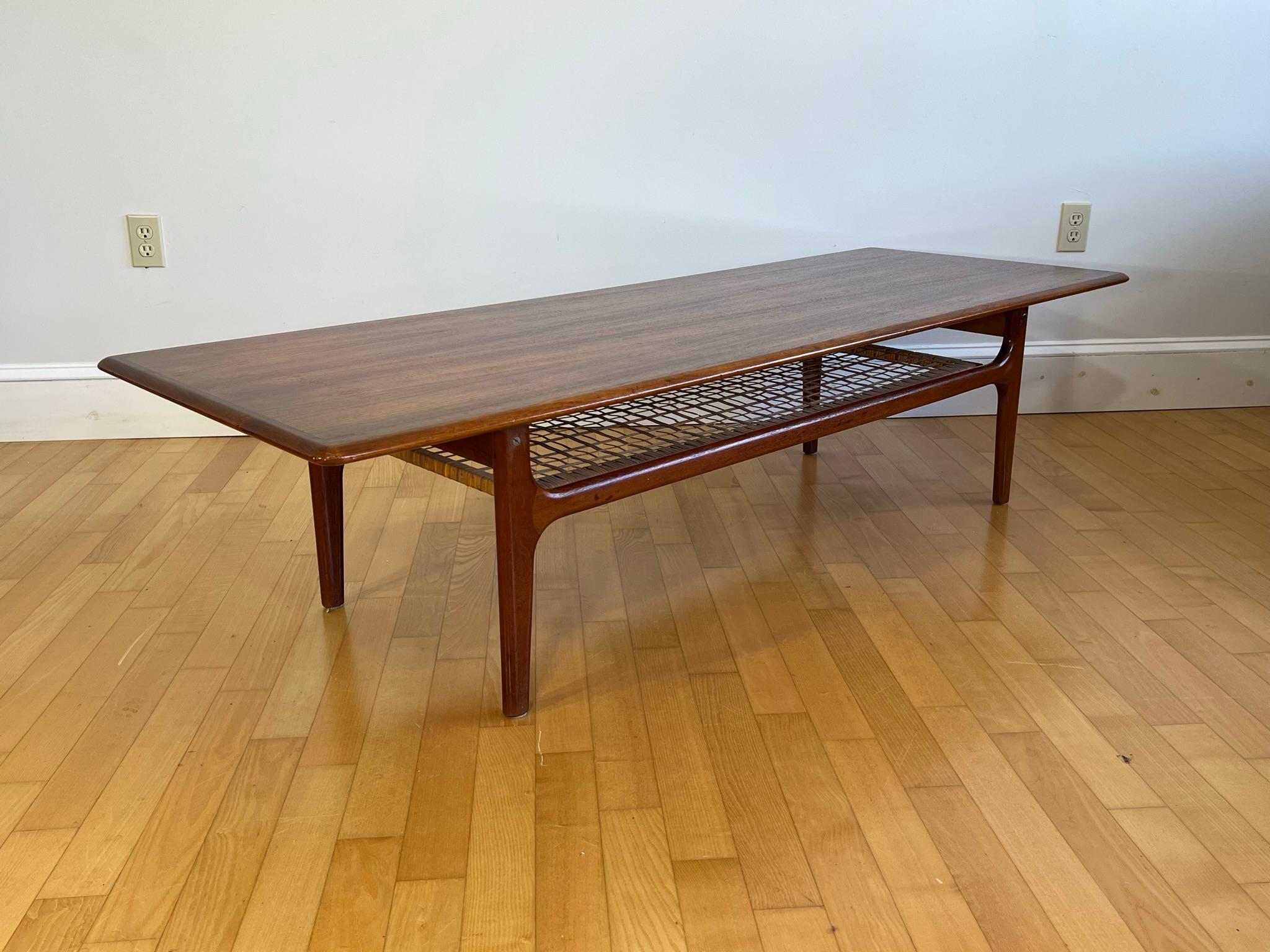 Fabulous vintage coffee table, made by renown danish company Trioh in the 60s. This gorgeous table consists of teak legs and upper plate and woven cane shelf.  It comes in a natural teak danish oil finish and timeless minimalist design. 
