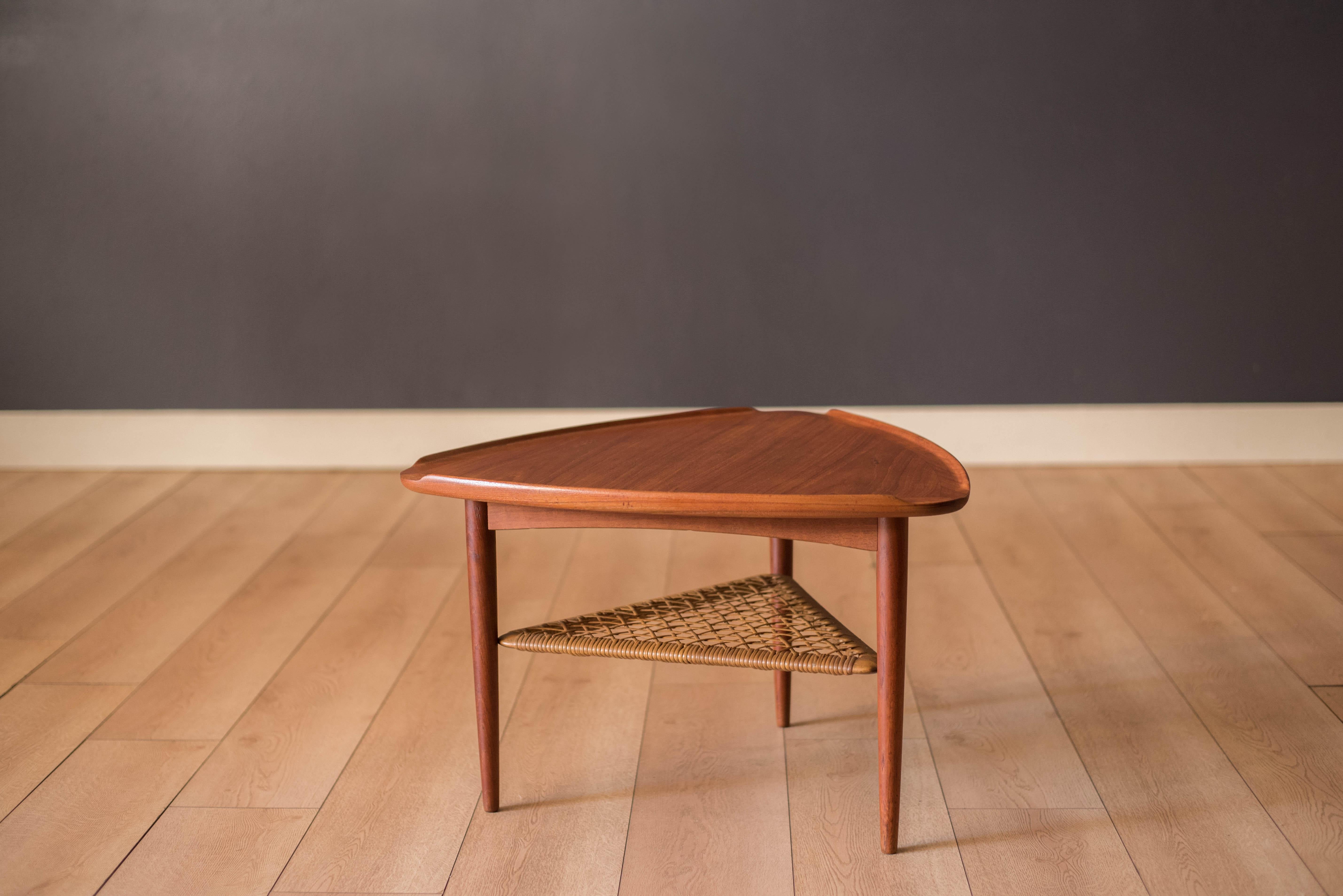 Mid Century triangular occasional guitar pick side table in teak designed by Poul Jensen imported by Selig, Denmark. This piece features a unique raised edge top and lower tier magazine shelf made of woven cane.

Lower tier shelf 8.25