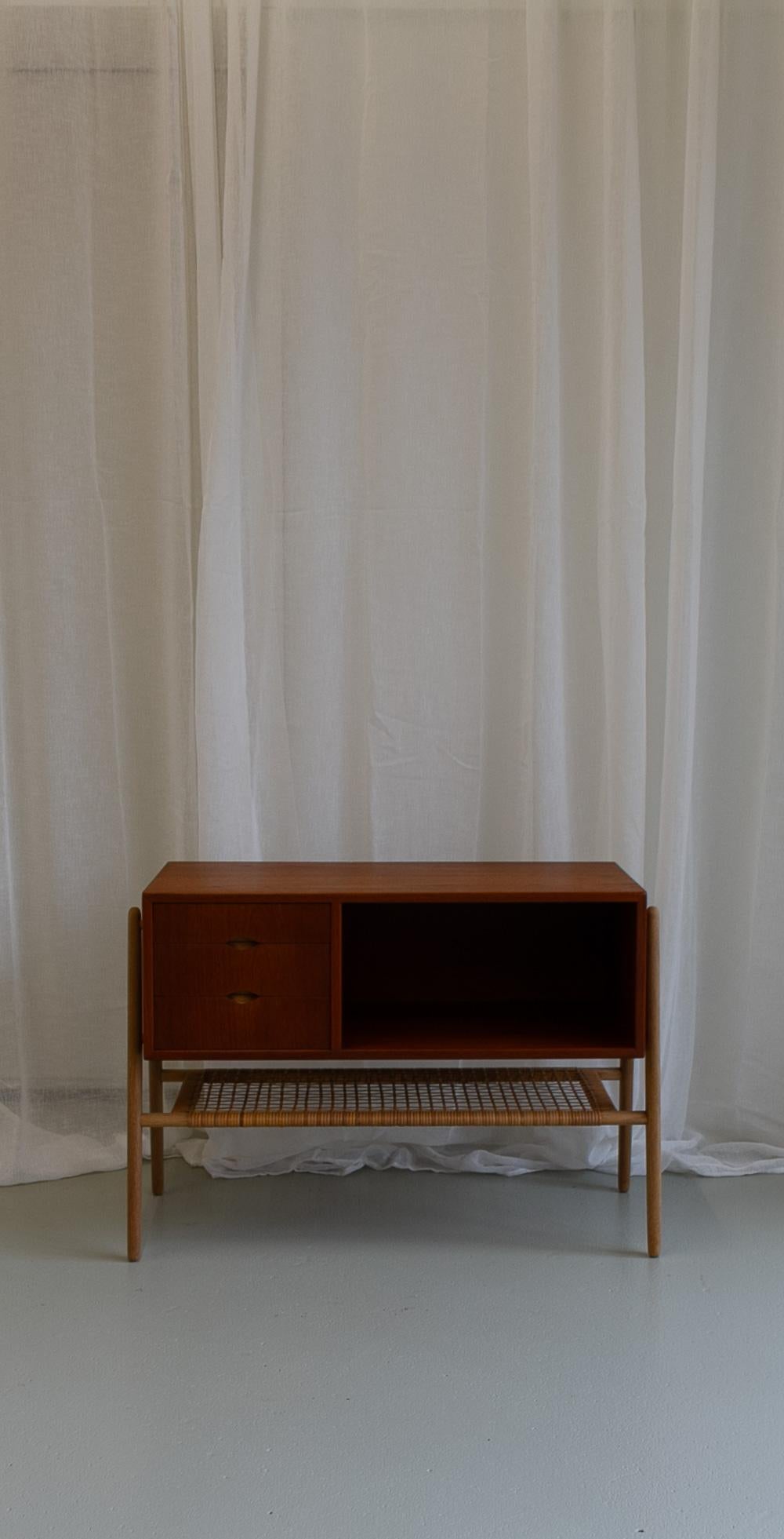 Danish Modern Teak and Oak Console Table with Cane Shelf, 1960s.

Danish Mid-Century Modern design small hall cabinet in teak and oak. Designed and manufactured by Valdemar Mortensen in Odense, Denmark. Three drawers and open shelf. Underneath is a