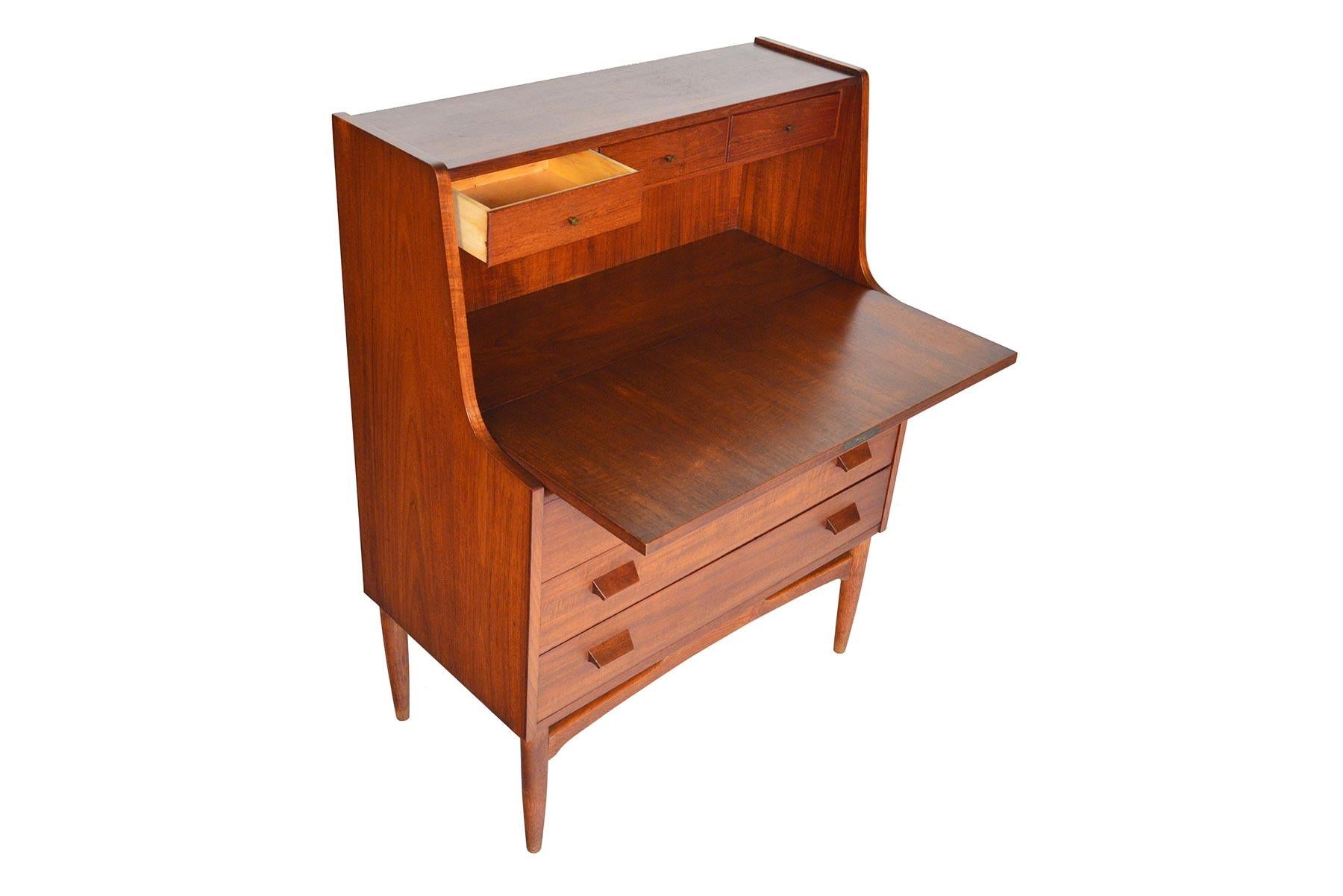 This lovely drop front Danish modern secretary desk in teak was manufactured in the 1960s. Offers spacious concealed storage and an easy to access workspace. When the door drops down, three small drawers are revealed. Three lower drawers offer