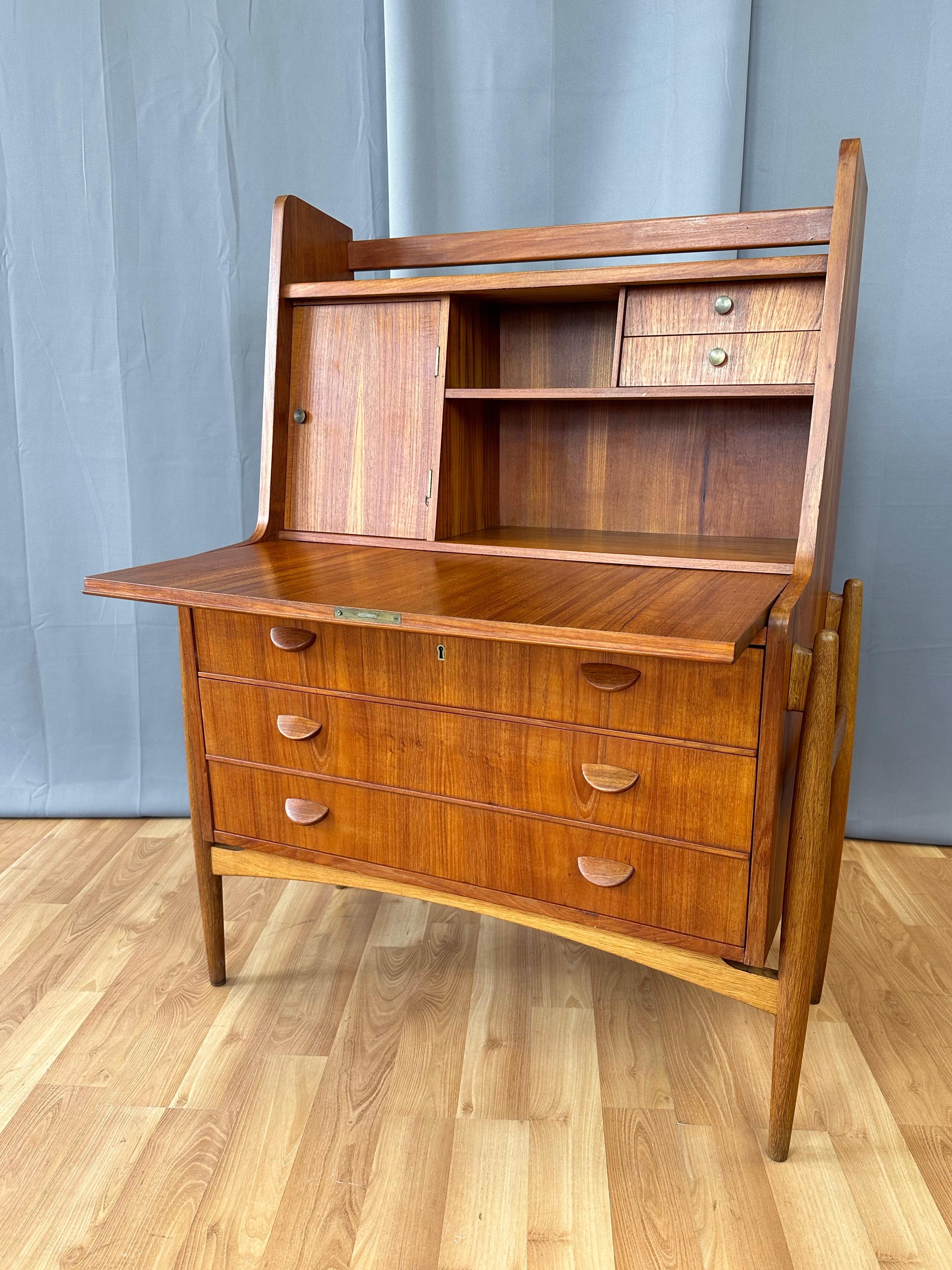An utterly charming and quite uncommon 1951 Scandinavian modern teak and oak drop-front secretary desk or vanity from Denmark.

Front drops down to serve as a nicely-sized work surface. Upper section with a mirror-backed door with brass pull at left