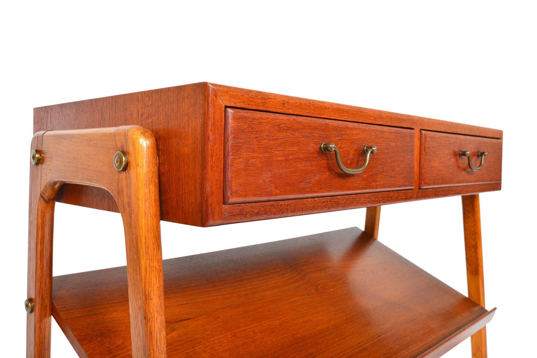 This Danish modern midcentury hallway chest with magazine rack is crafted in teak and oak. The beautifully cornered case holds two drawers with patinated brass pulls. The exterior mounted oak base supports the case and a canted rack perfect for