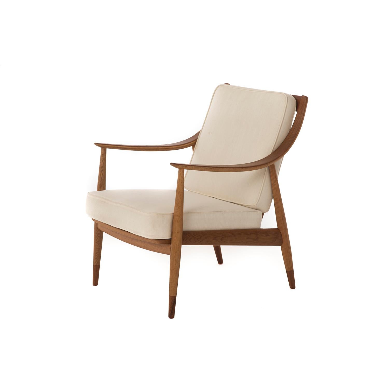 This Scandinavian Mid-Century Modern lounge chair features a sweeping arm and mid-height spindle back. The frame is a combination of oiled teak and oak that is elegant and timeless. Sprung removable cushions are upholstered in a bone white