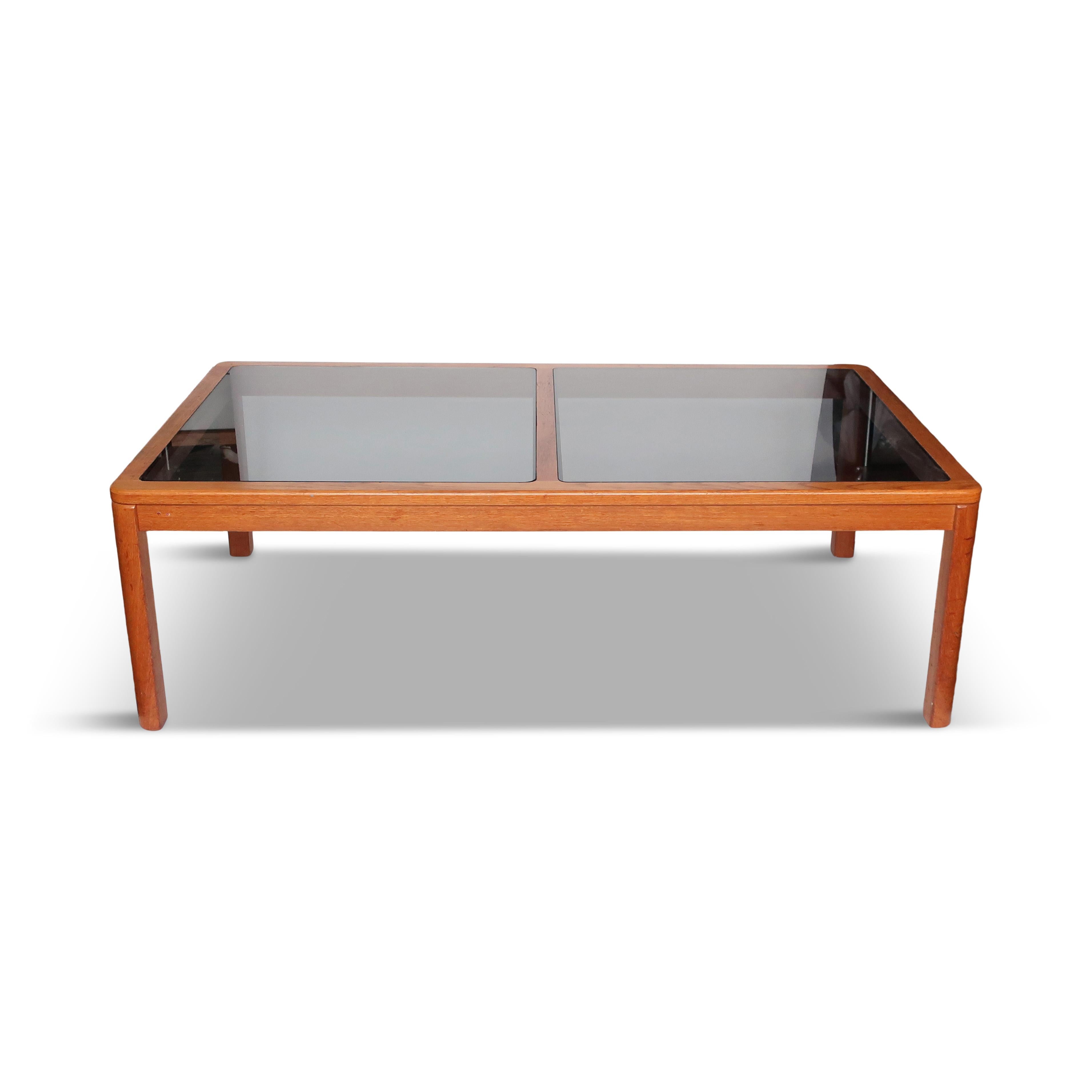 Lovely Mid-Century Modern teak and smoked glass coffee table by Danish furniture manufacturer Uldum Mobelfabrik. Solid teak frame with rounded corners that soften the table's feel and two pieces of smoked glass inset to form the table top. Sleek and
