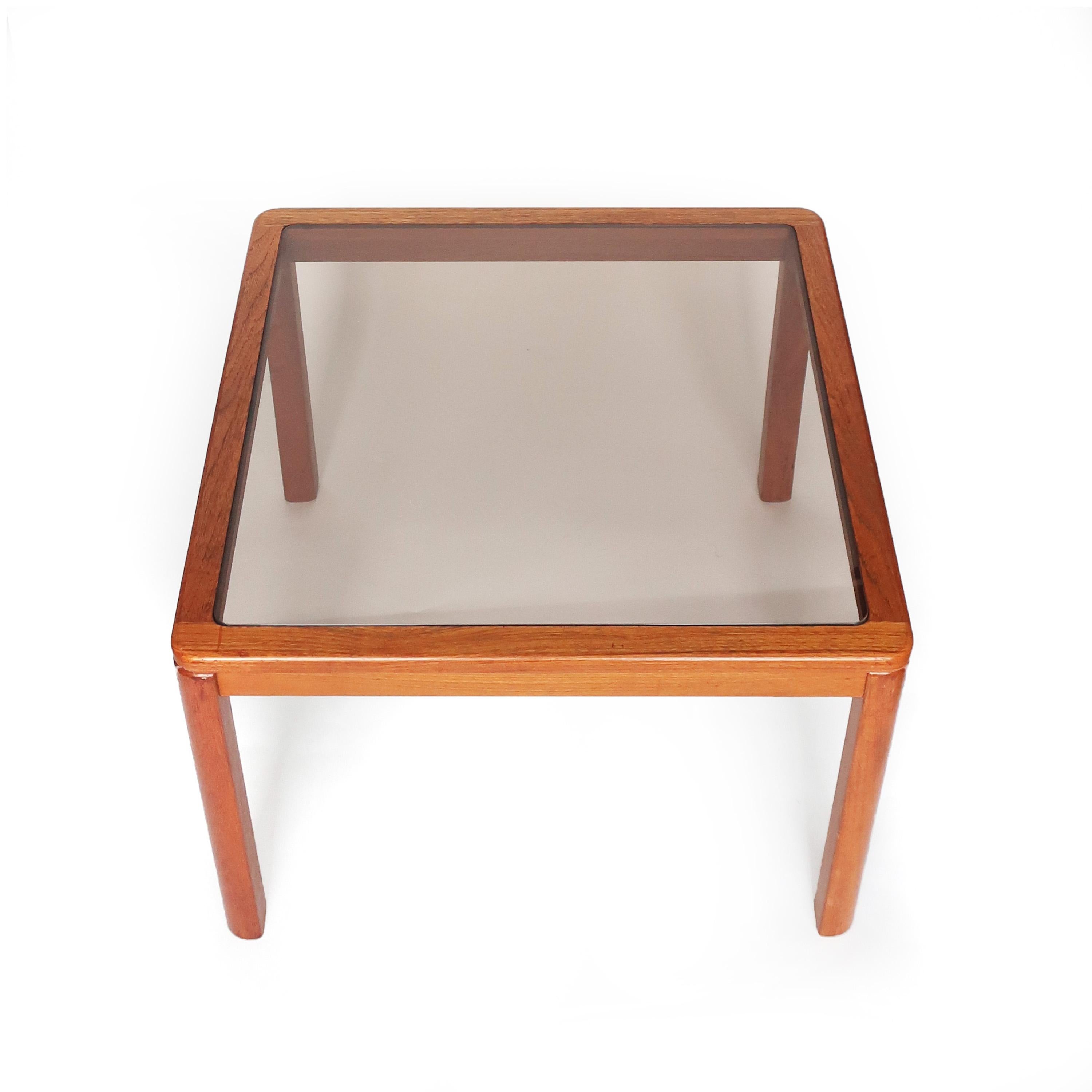 Lovely Mid-Century Modern teak and smoked glass end or side table by Danish furniture manufacturer Uldum Mobelfabrik. Solid teak frame with rounded corners that soften the table's feel and a piece of smoked glass inset to form the table top. Sleek