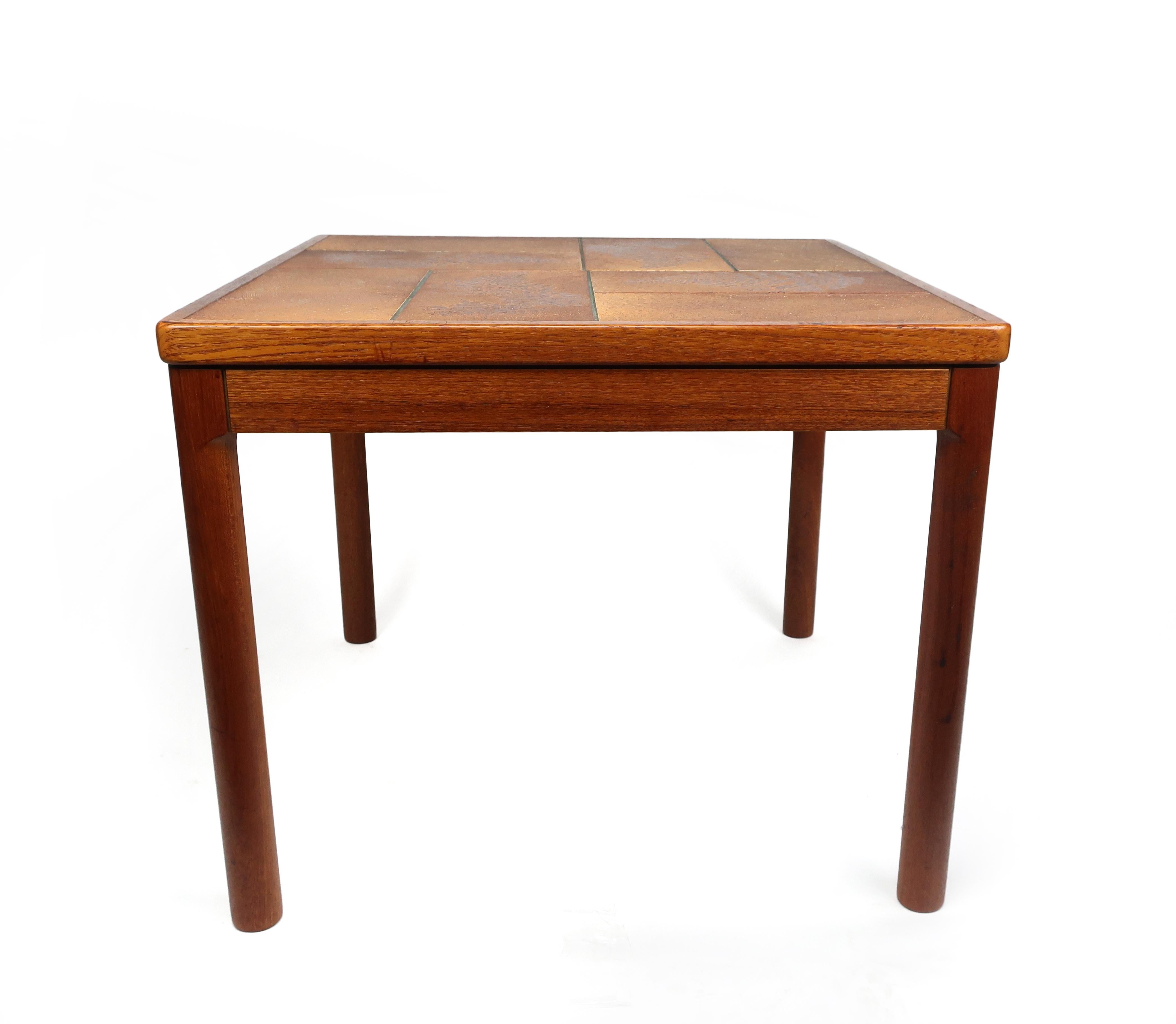 A vintage Danish modern teak and tile side table with lovely round turned legs by Trioh. The tabletop's tile has an orange and brown glaze, a pattern of fern leaves, and etched decoration. Eight tiles in total.

In excellent vintage condition with